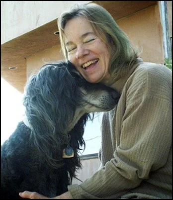 A woman hugging and kissing a black and white dog that is licking her face, both appearing happy.
