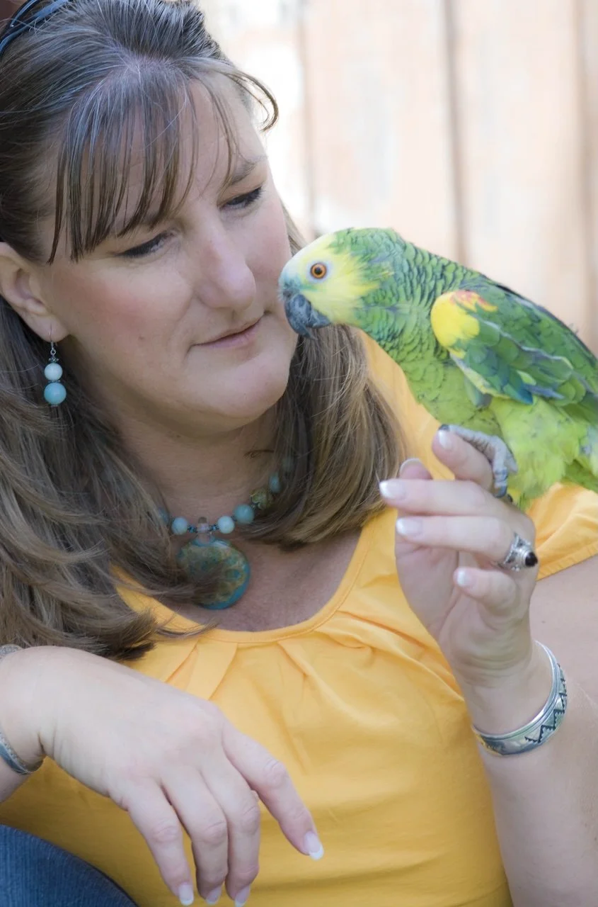 A woman holding a green and yellow parrot close to her face, looking at it affectionately.