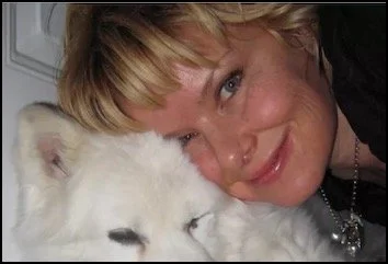 A woman smiling with her face close to a white dog, possibly a husky, with closed eyes.