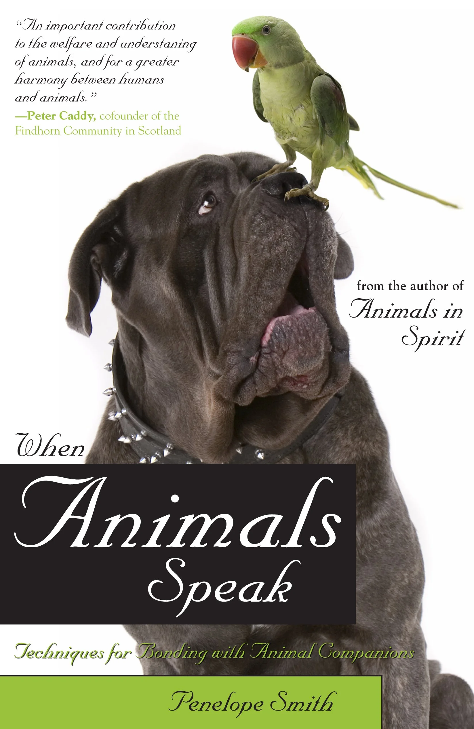 The cover of a book titled "Animals Speak" features a large dog with a spiked collar and a green bird, likely an Amazon parrot, perched on the dog's face. The title appears in large cursive text, with additional text indicating the author is Penelope Smith and includes a quote from Peter Caddy about the importance of animals in fostering harmony between humans and animals.