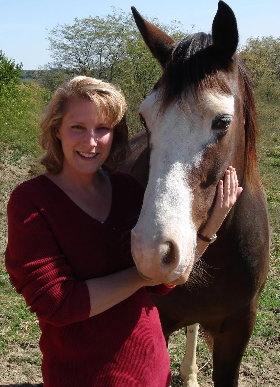 A woman hugging a brown and white horse outdoors on a sunny day.