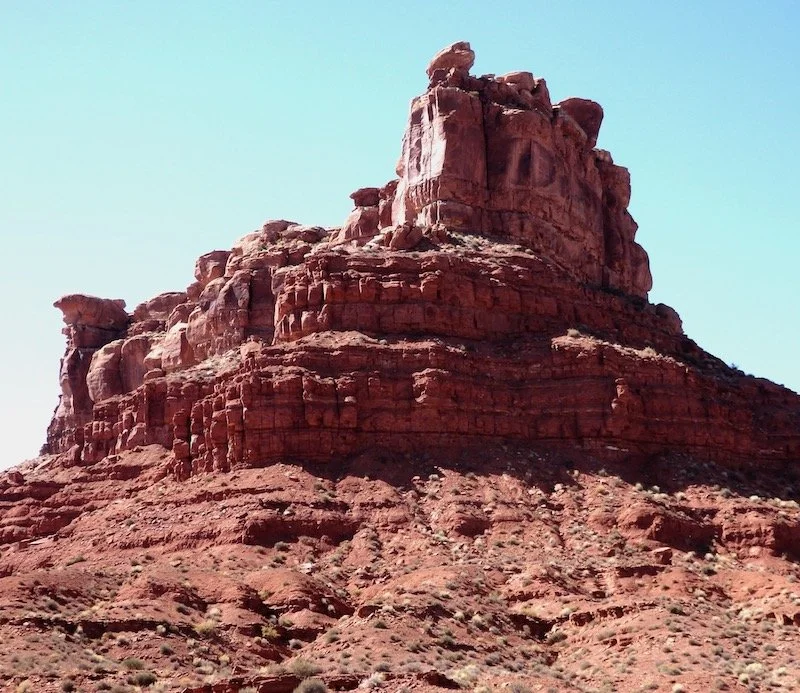 Large red rock formation in a desert landscape with a clear sky.
