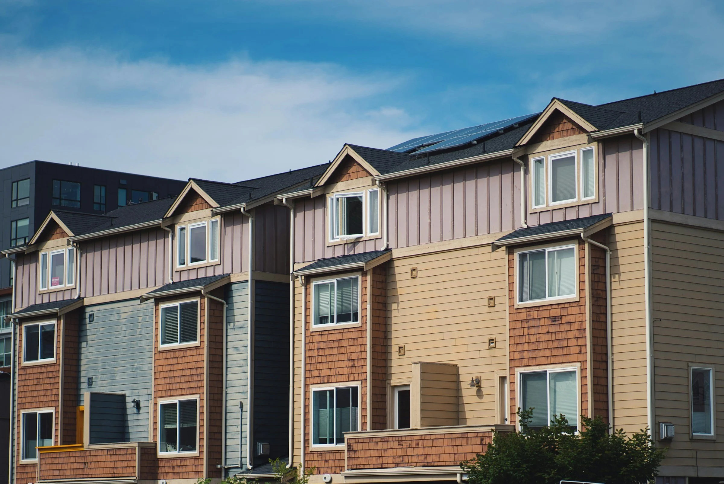 Multiple colorful townhouses with pitched roofs, some with solar panels, under a blue sky with a few clouds.
