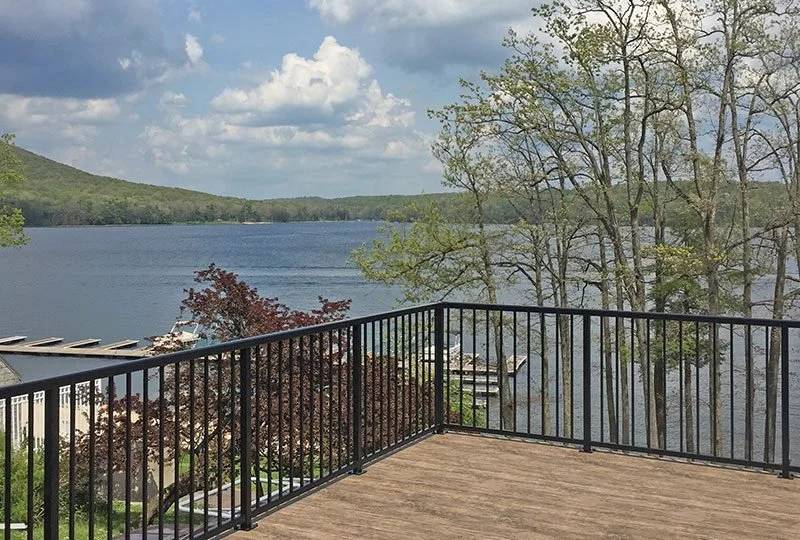 View from a deck overlooking a lake with trees and hills in the background, under partly cloudy sky.