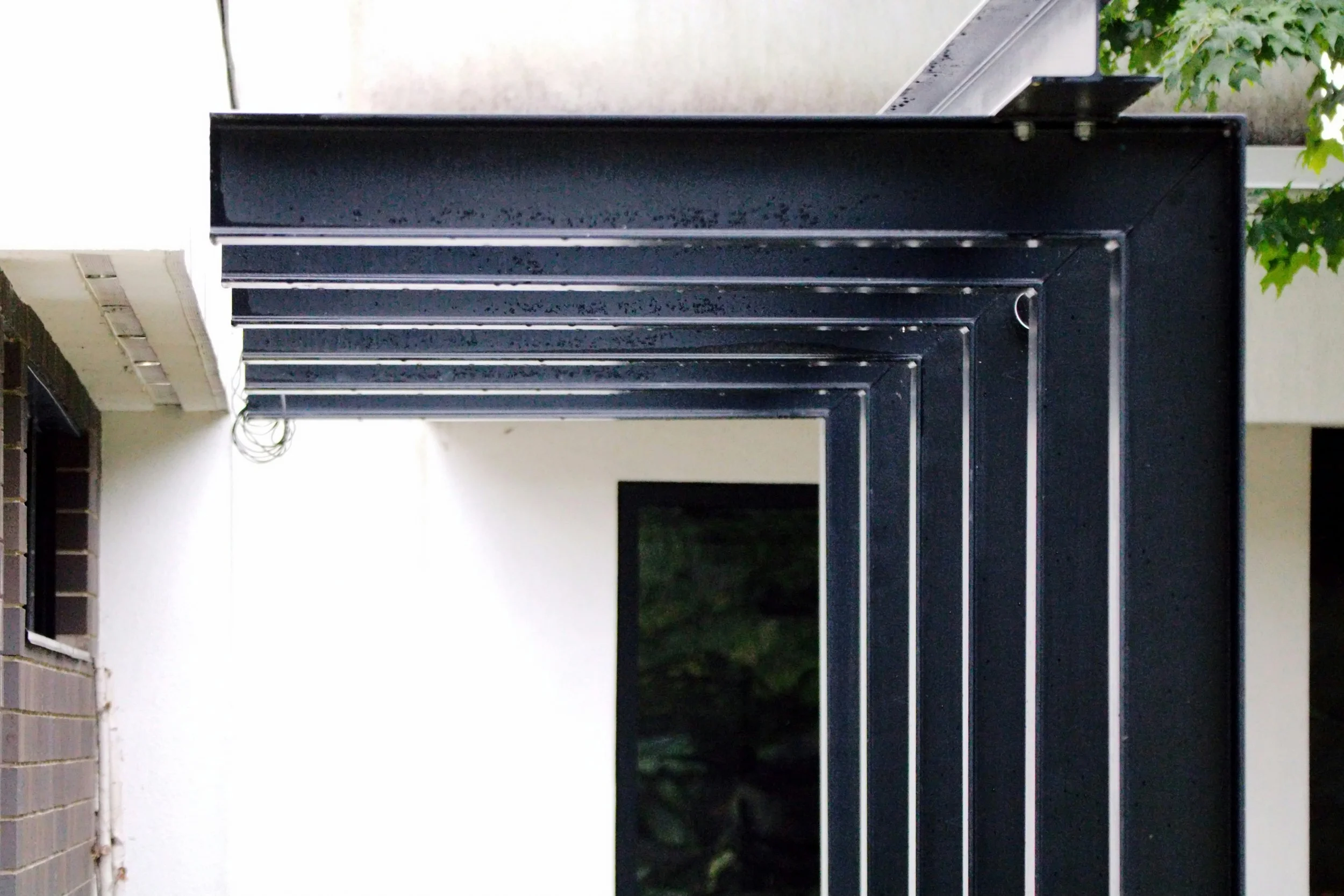 A series of black metal doors aligned near a white wall, with a small green plant in the upper right corner and some wires hanging from the ceiling.