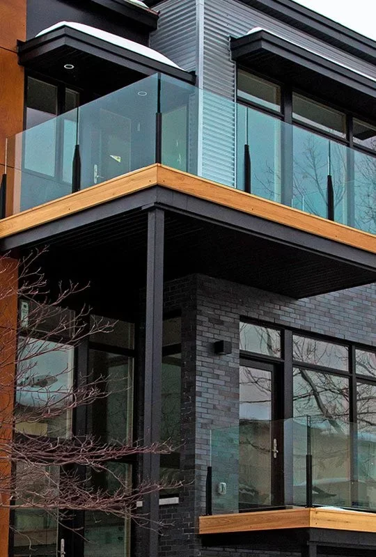 Close-up of a modern multi-story building with glass balconies, black brick exterior, and wooden trim.