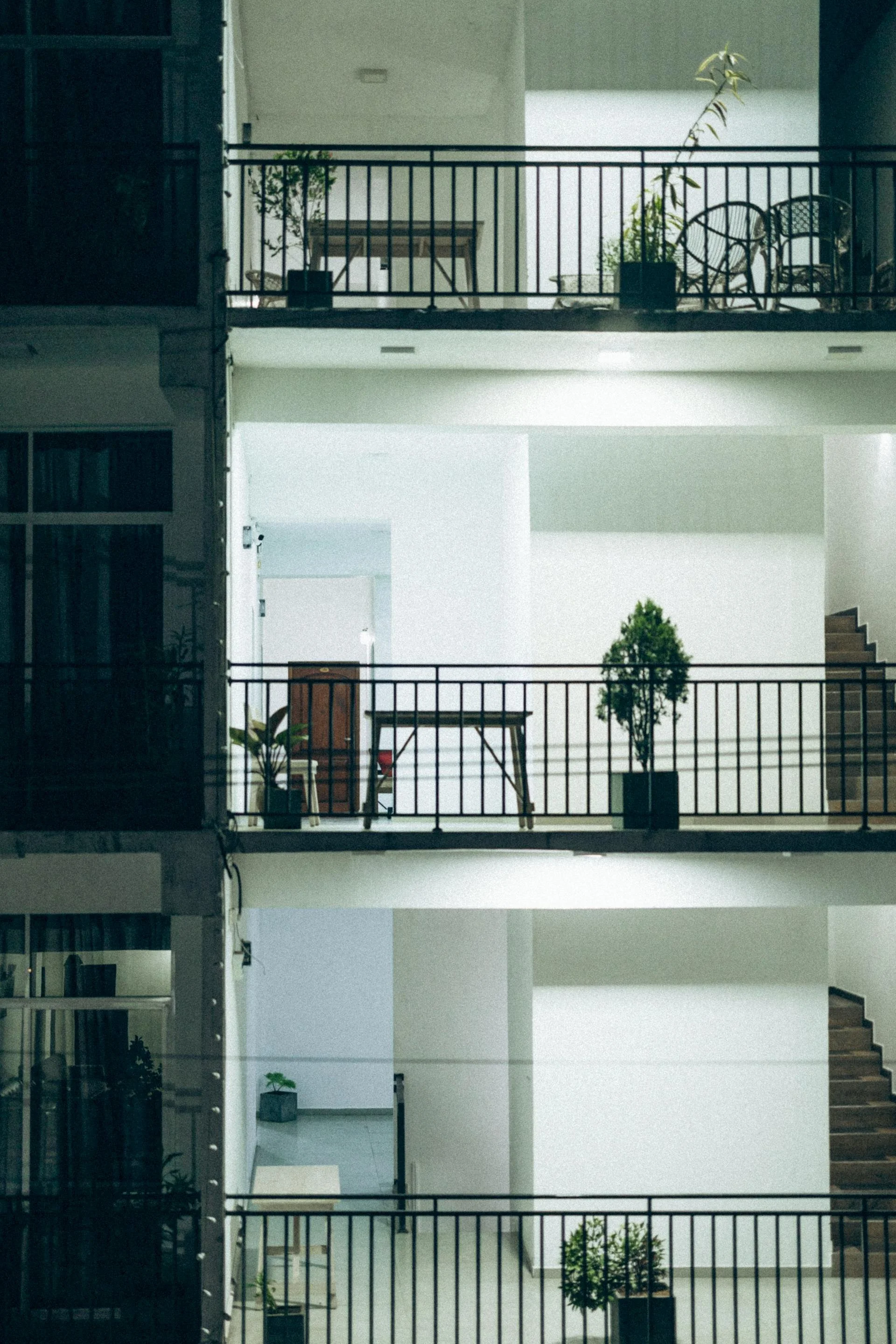 Multiple levels of a modern apartment building with balconies, patio furniture, potted plants, and stairs, seen at night with interior lighting.