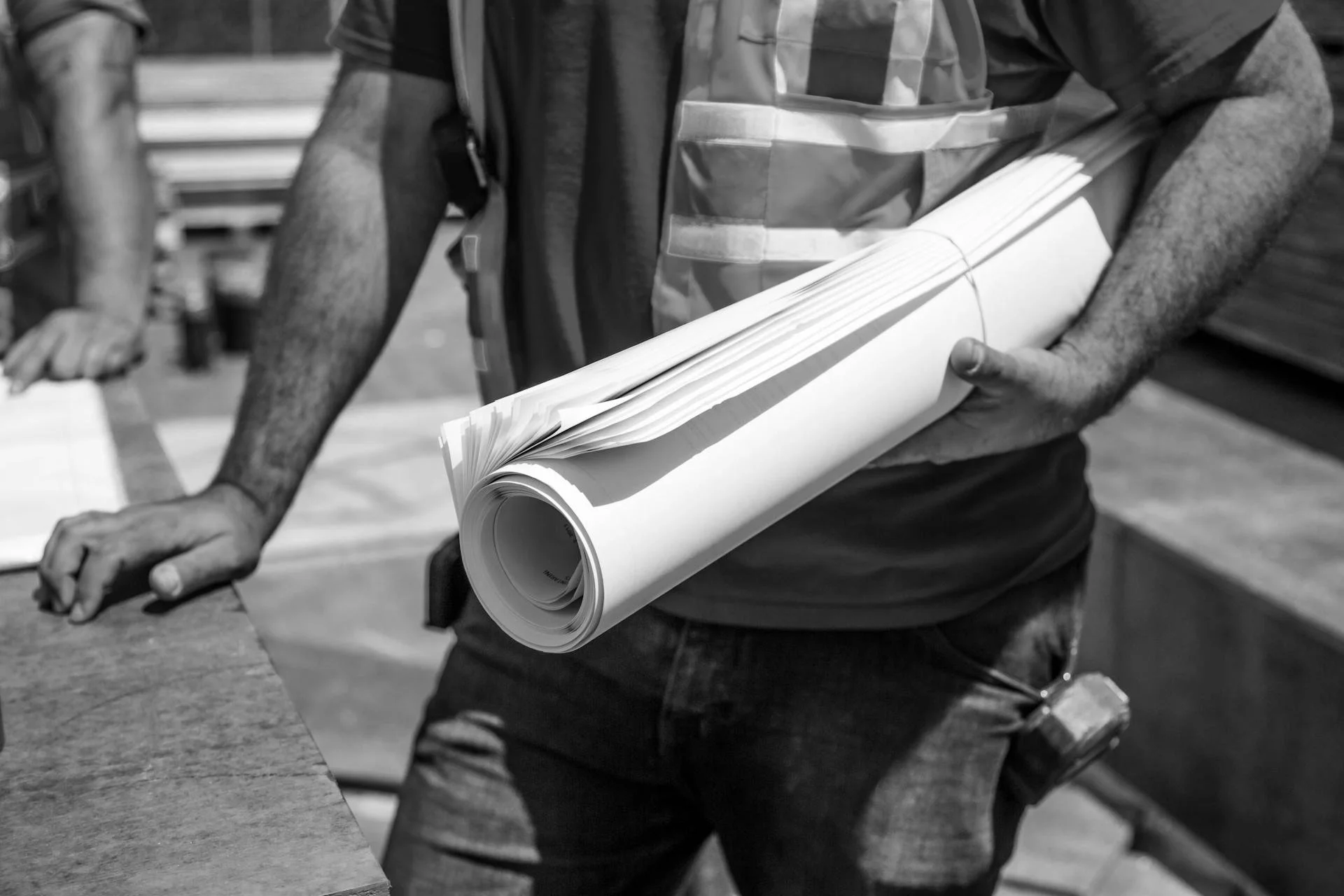 Person holding rolled-up blueprint at a construction site in black and white.