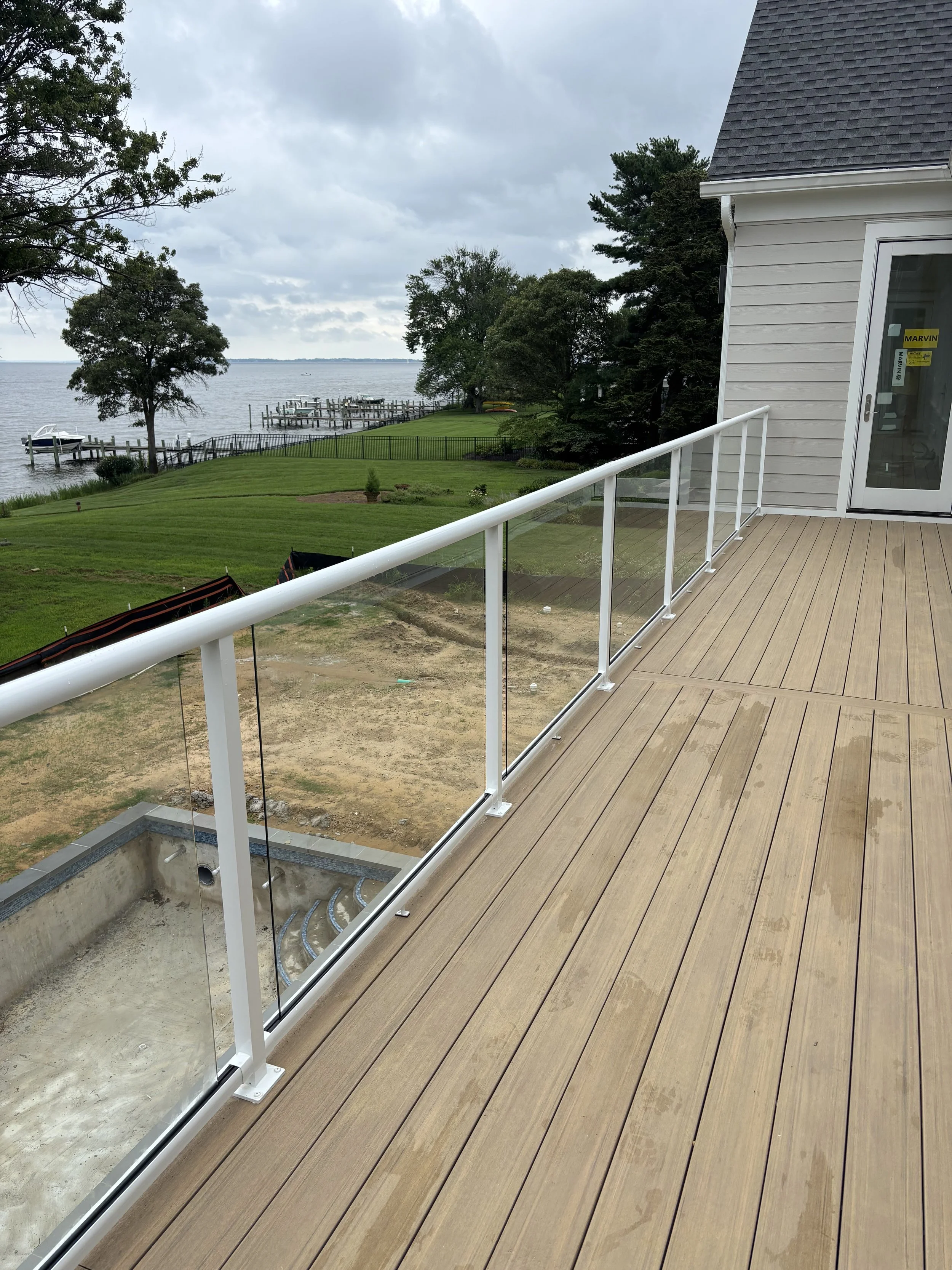 View from a balcony overlooking a grassy yard with trees and a body of water with docks and boats on a cloudy day.