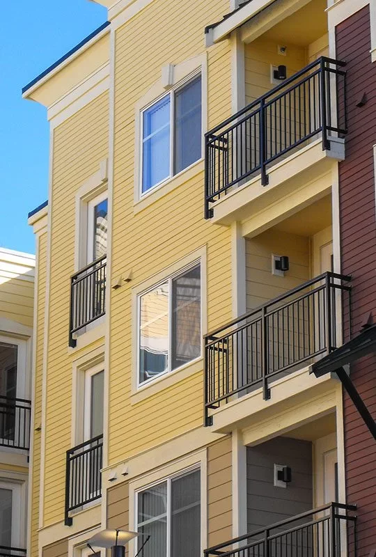 Exterior of a multi-story yellow apartment building with black metal balconies and white-framed windows.