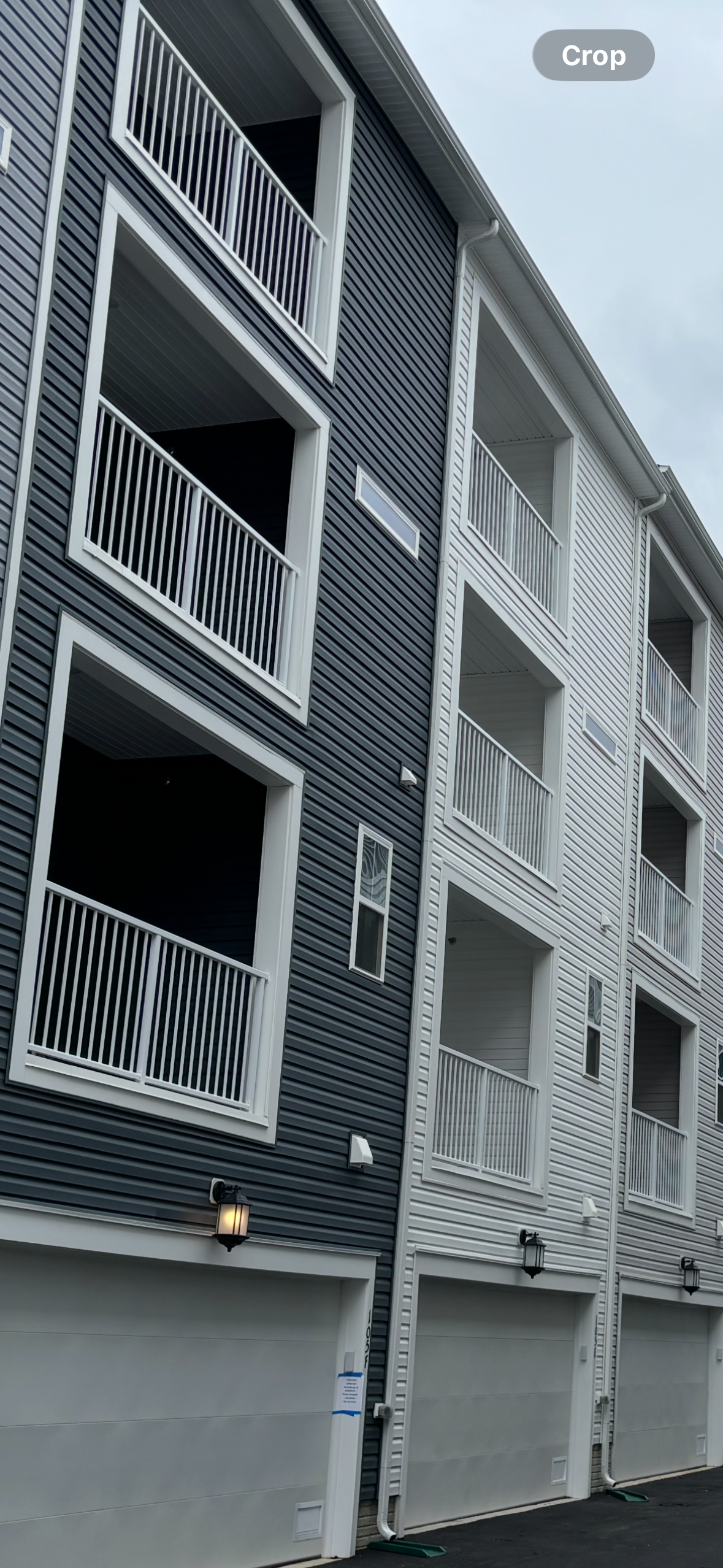 Multi-story residential building with white balconies, gray and white exterior siding, and garage doors at ground level.