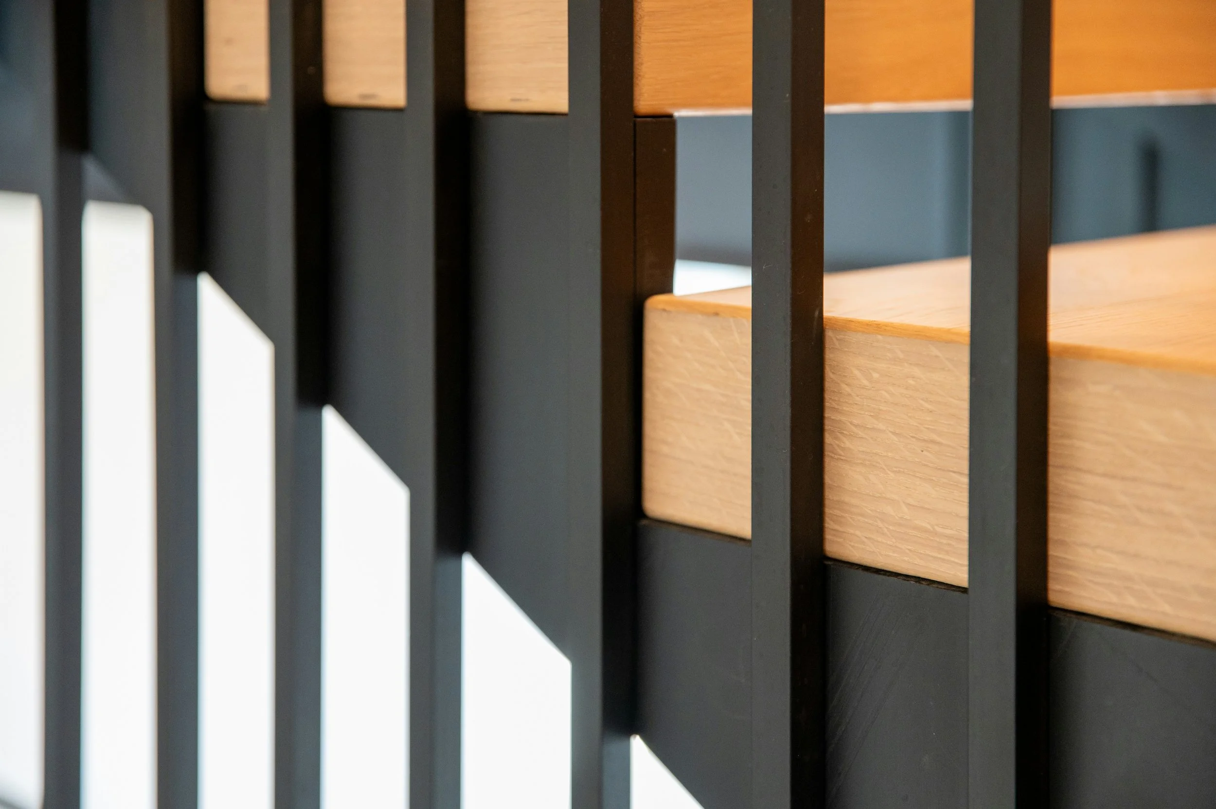 Close-up of a modern wooden and metal railing with vertical black metal bars and rectangular wooden inserts.