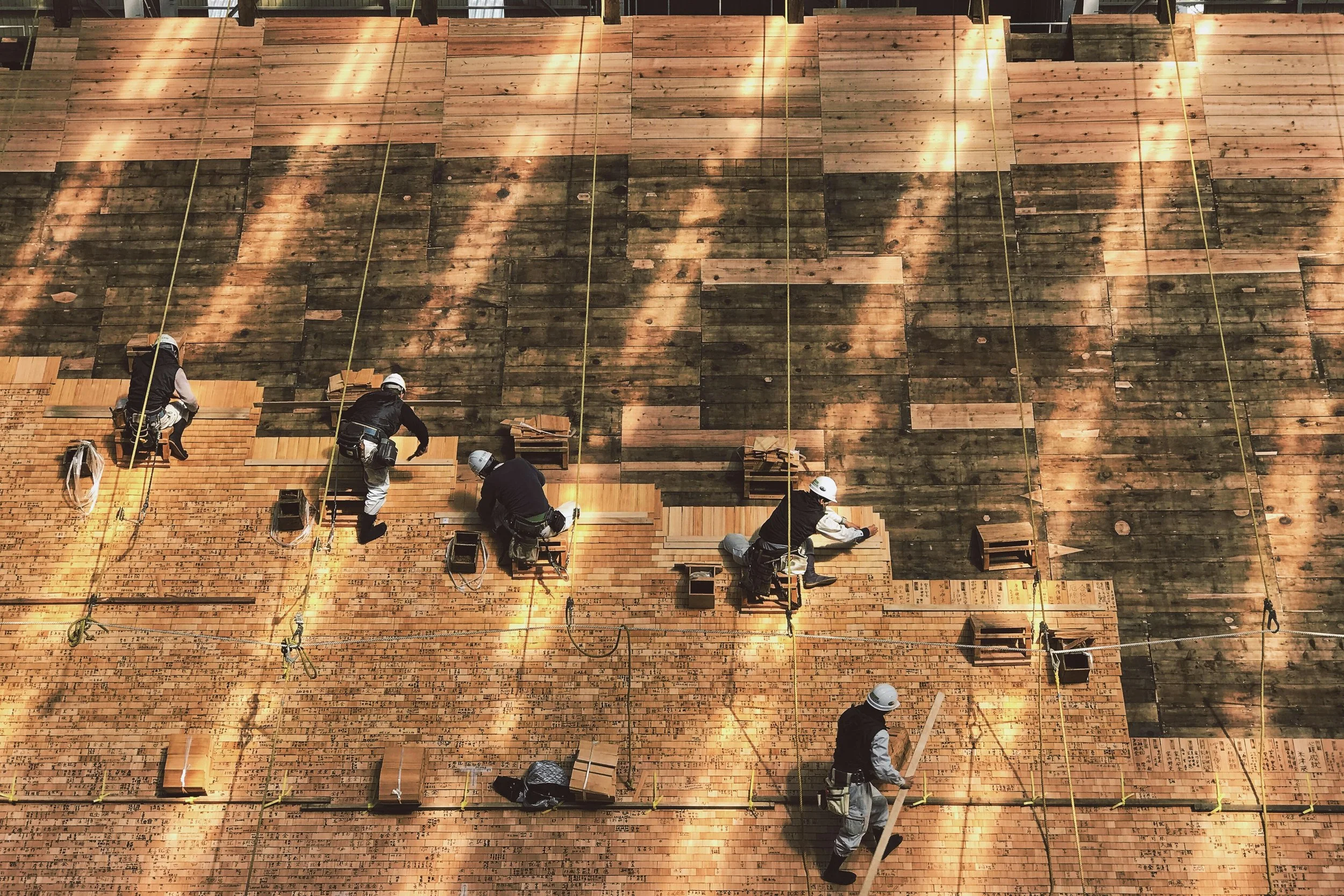 Construction workers installing wooden flooring on a large wall, with scaffolding and safety helmets.