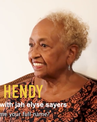 Headshot of Lynn smiling on a white background. Lynn is wearing a black and copper patterned shirt. Her hair is colored blonde.