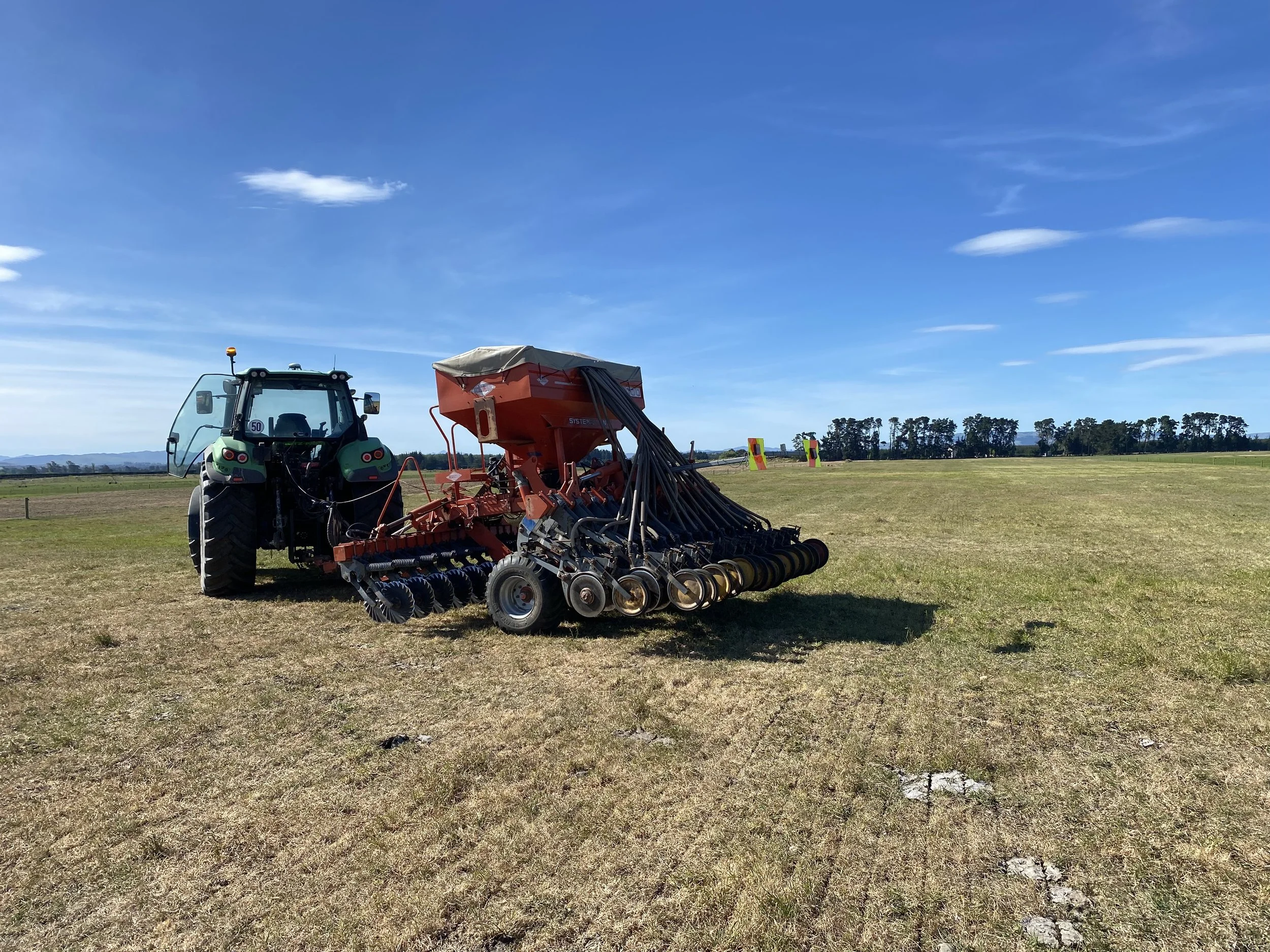 A tractor in an open field with equipment attached, under a bright blue sky with a few clouds.
