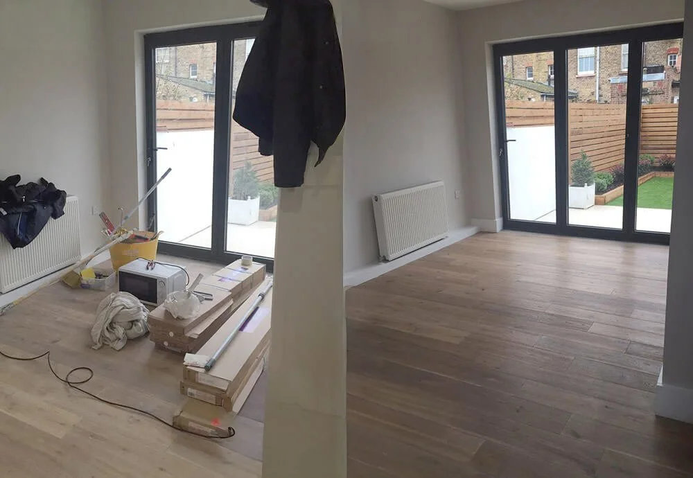 Empty room with large glass doors leading to a patio, partially furnished with construction materials and tools, including a microwave, boxes, and hanging clothes.