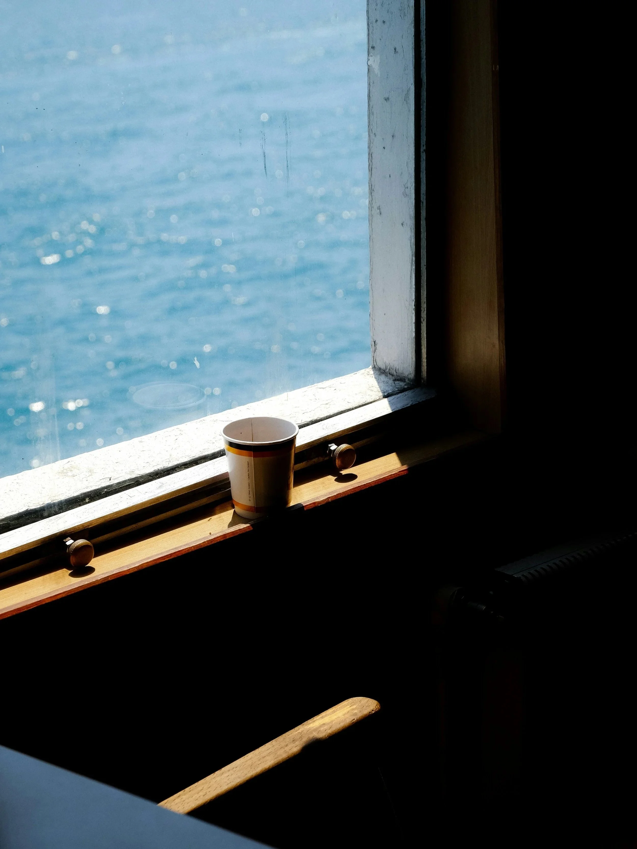 A coffee cup placed on a windowsill with a view of the ocean outside.