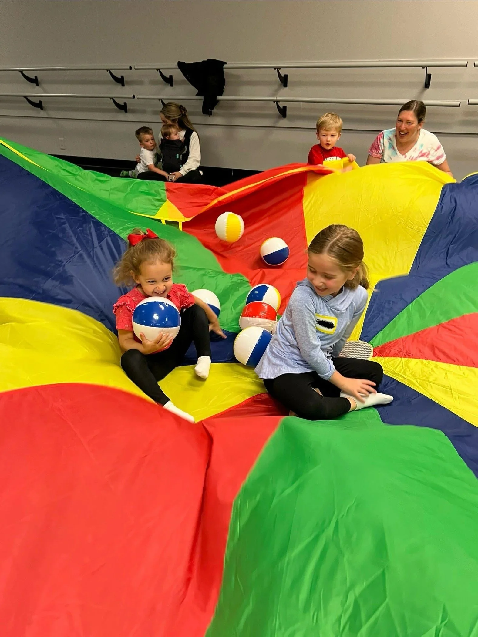 two girls having fun in the middle of a play parachute