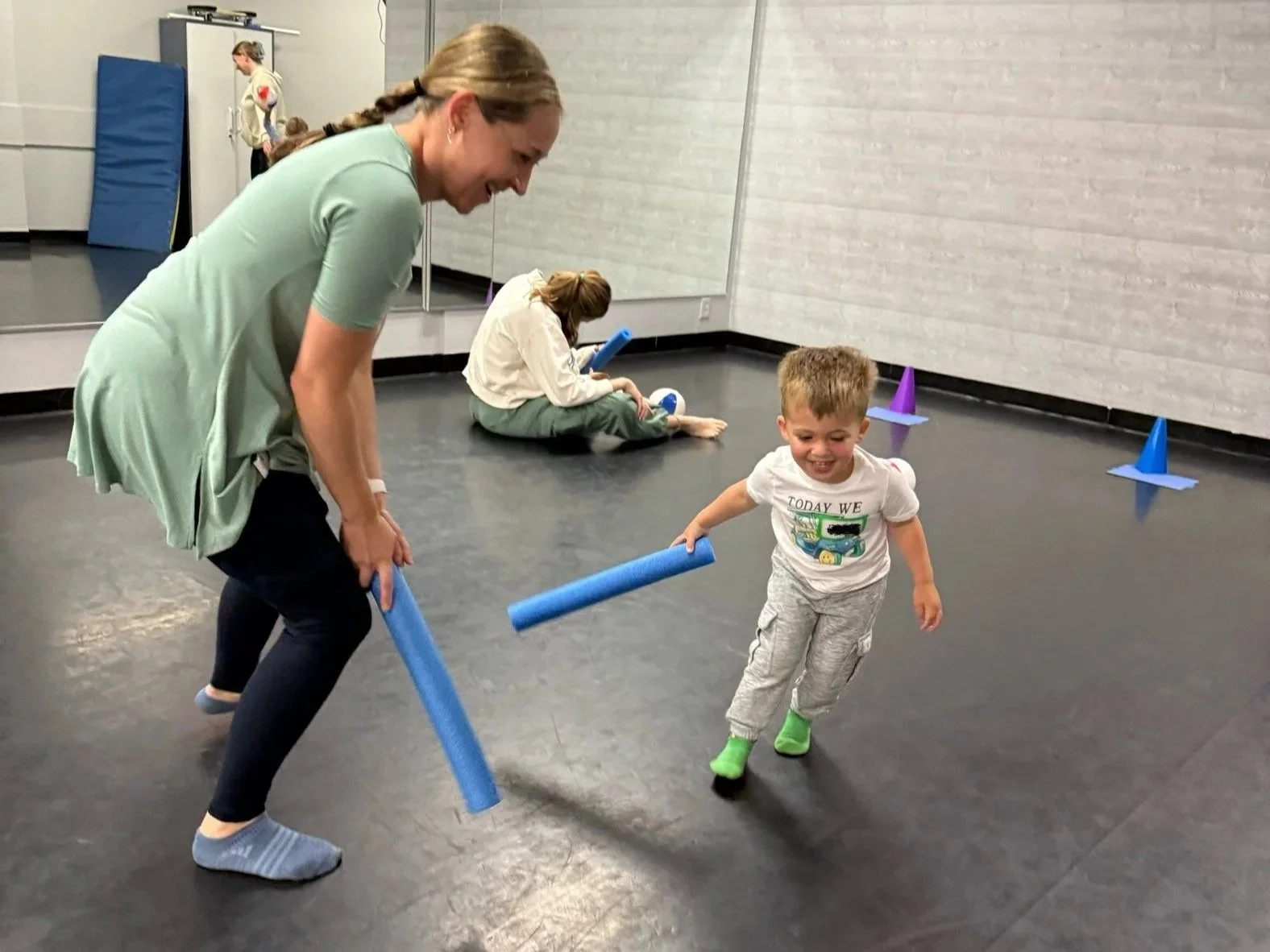 a teacher and child playing hockey with pool noodles and a soft ball