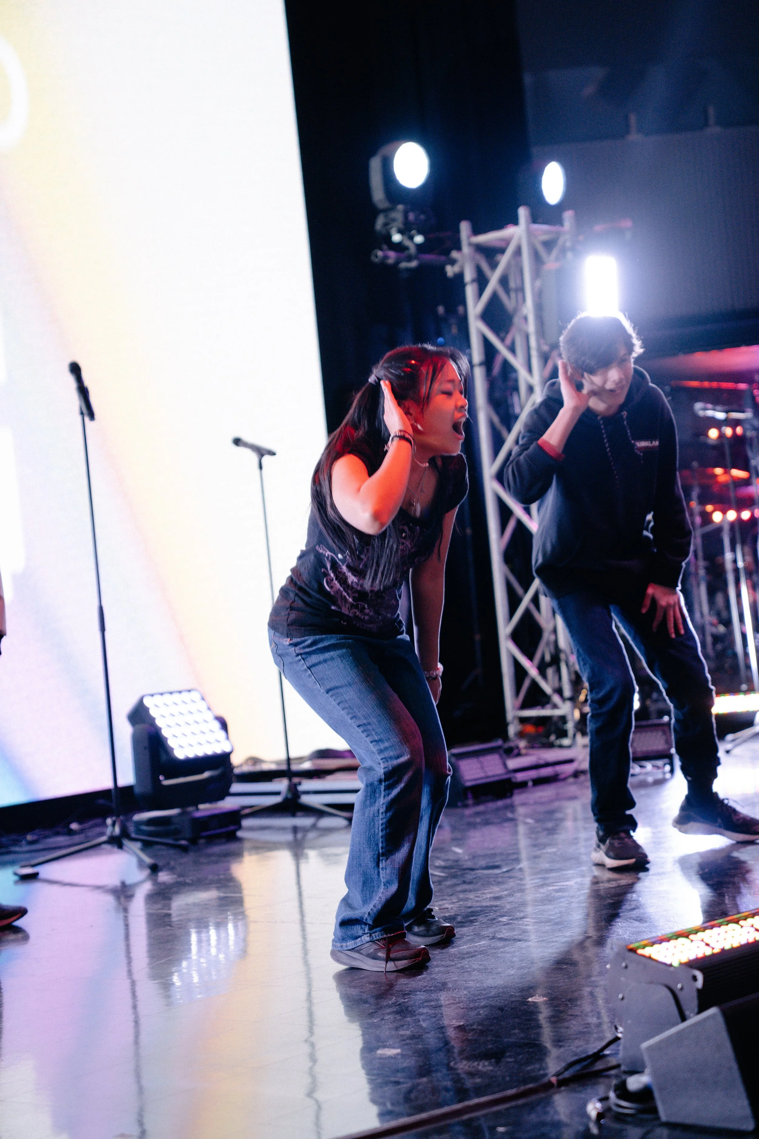 Two people dancing on stage with microphones, stage lights, and equipment around them.