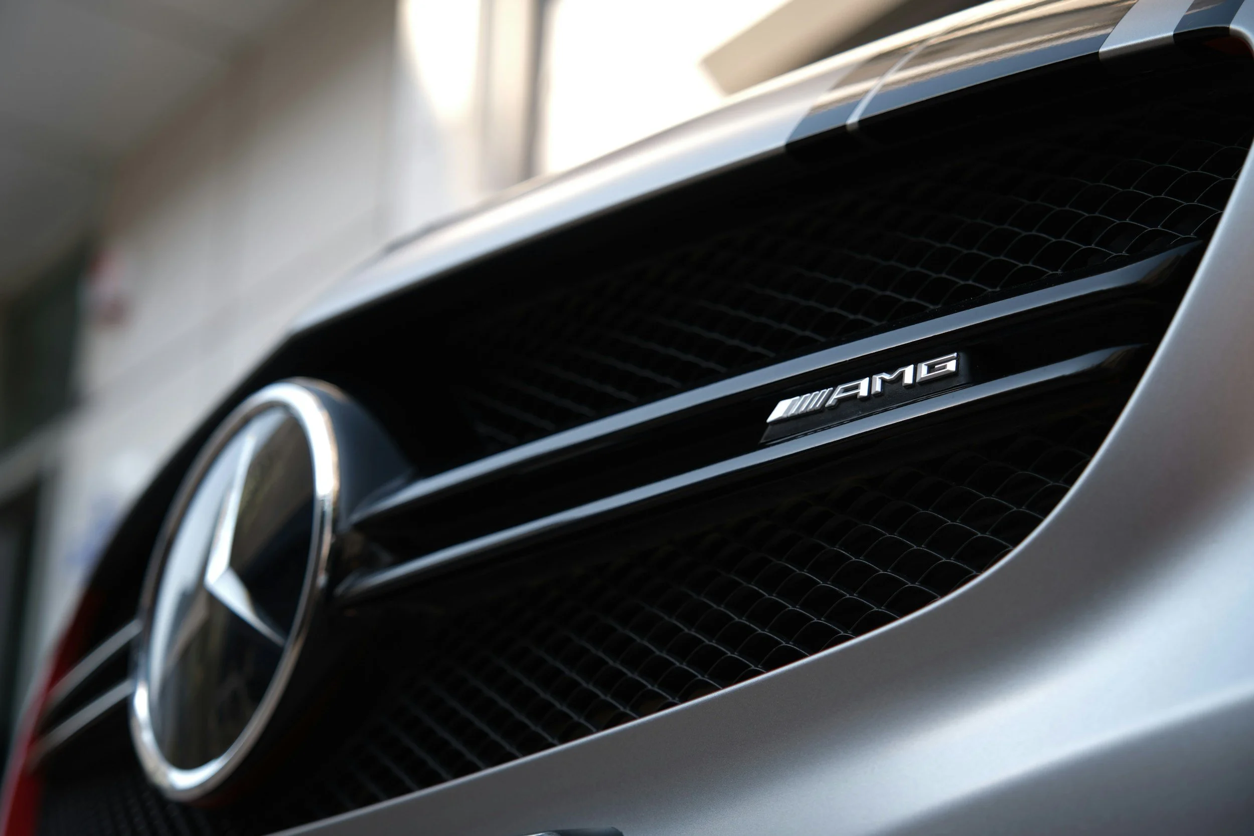 Close-up of a Mercedes-AMG car grille showing the AMG badge and the Mercedes logo in silver and black.
