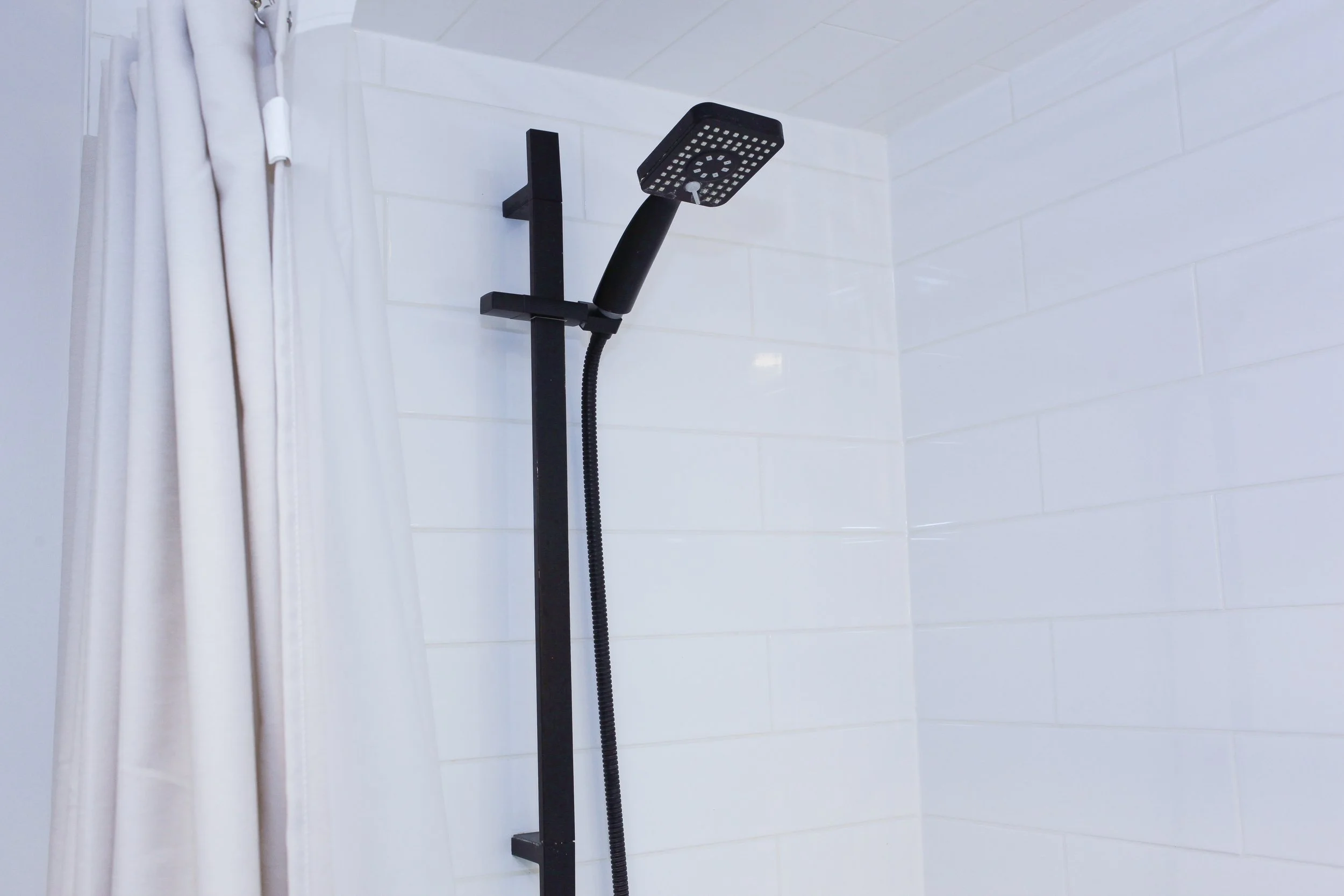 Black shower panel with adjustable rainfall showerhead mounted on a white tiled bathroom wall.