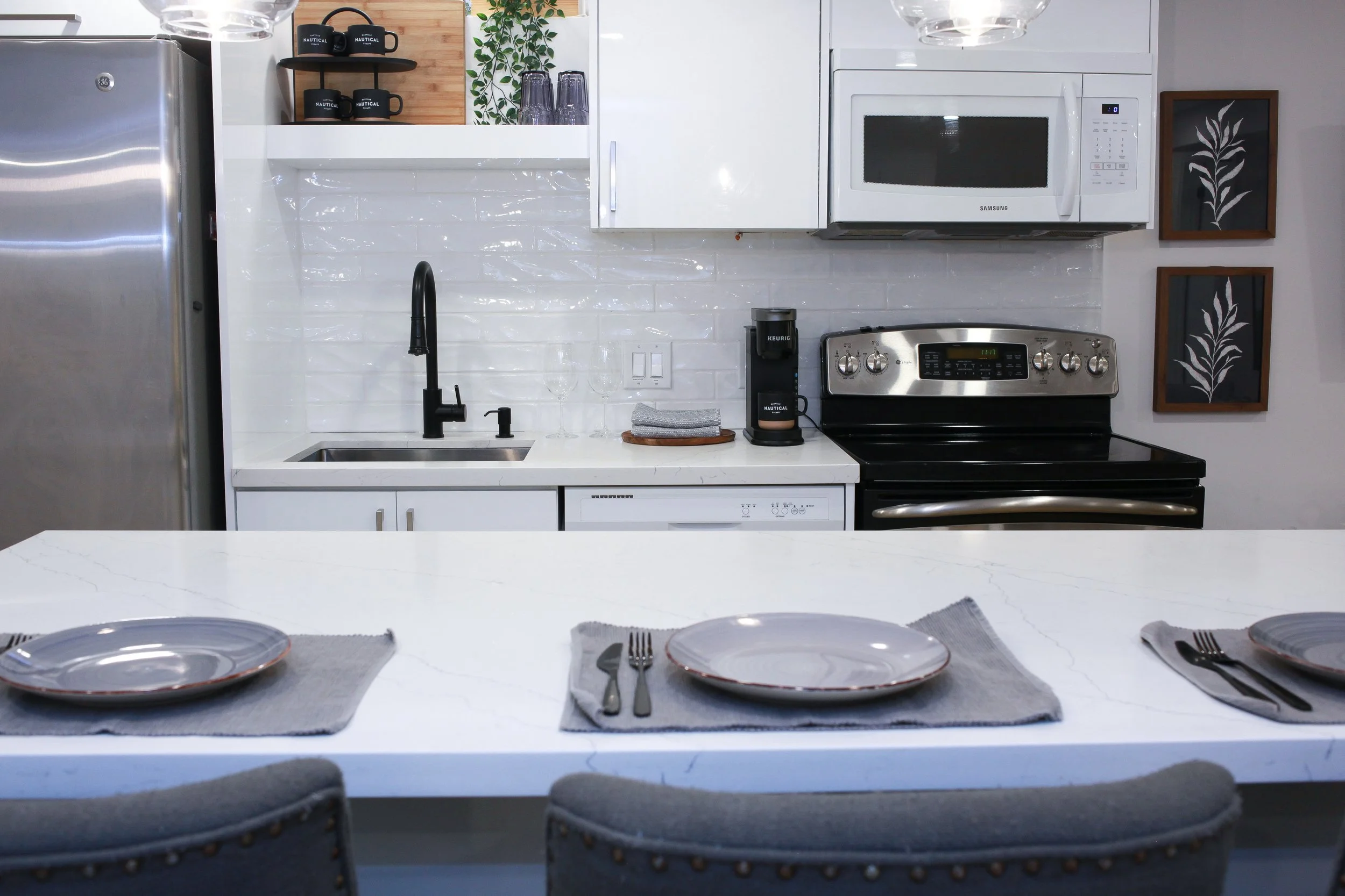 Modern kitchen with white cabinetry, black faucet, stainless steel appliances, and a white marble countertop with place settings.