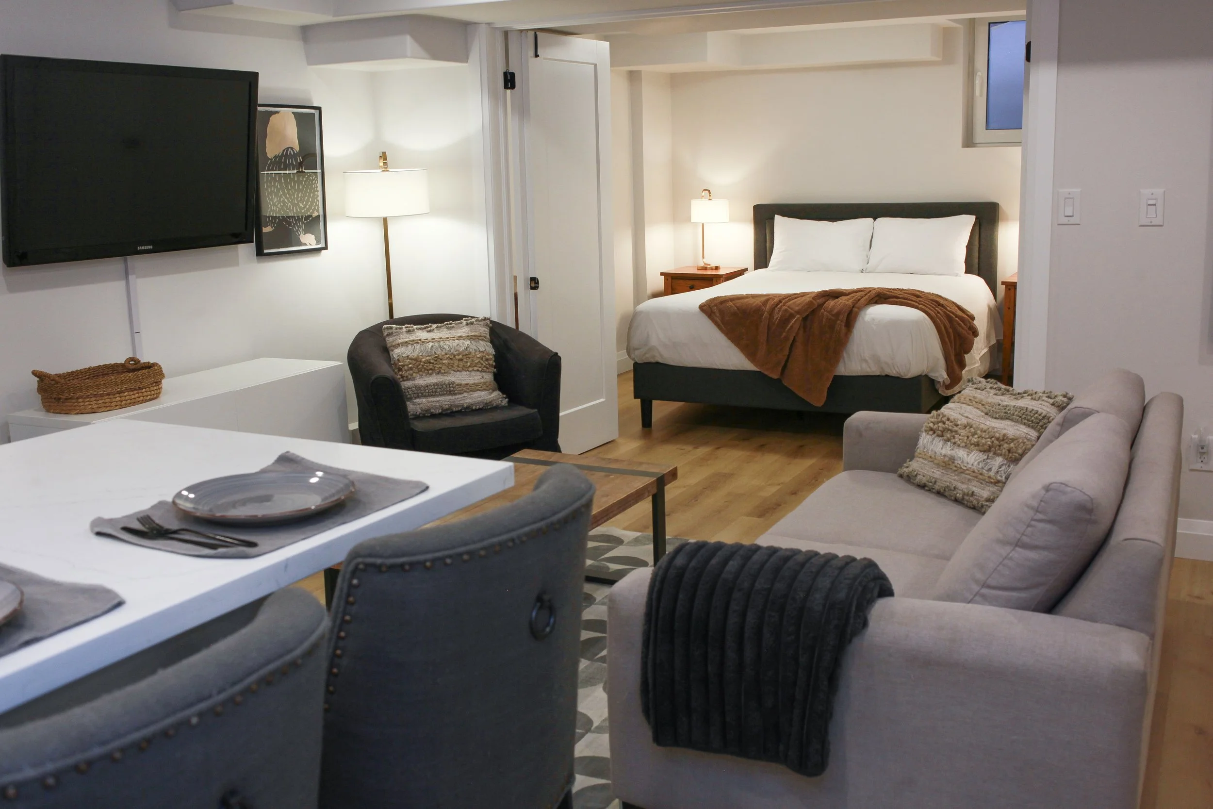 Interior of a modern studio apartment with a bed, sofa, dining table, and TV on the wall.