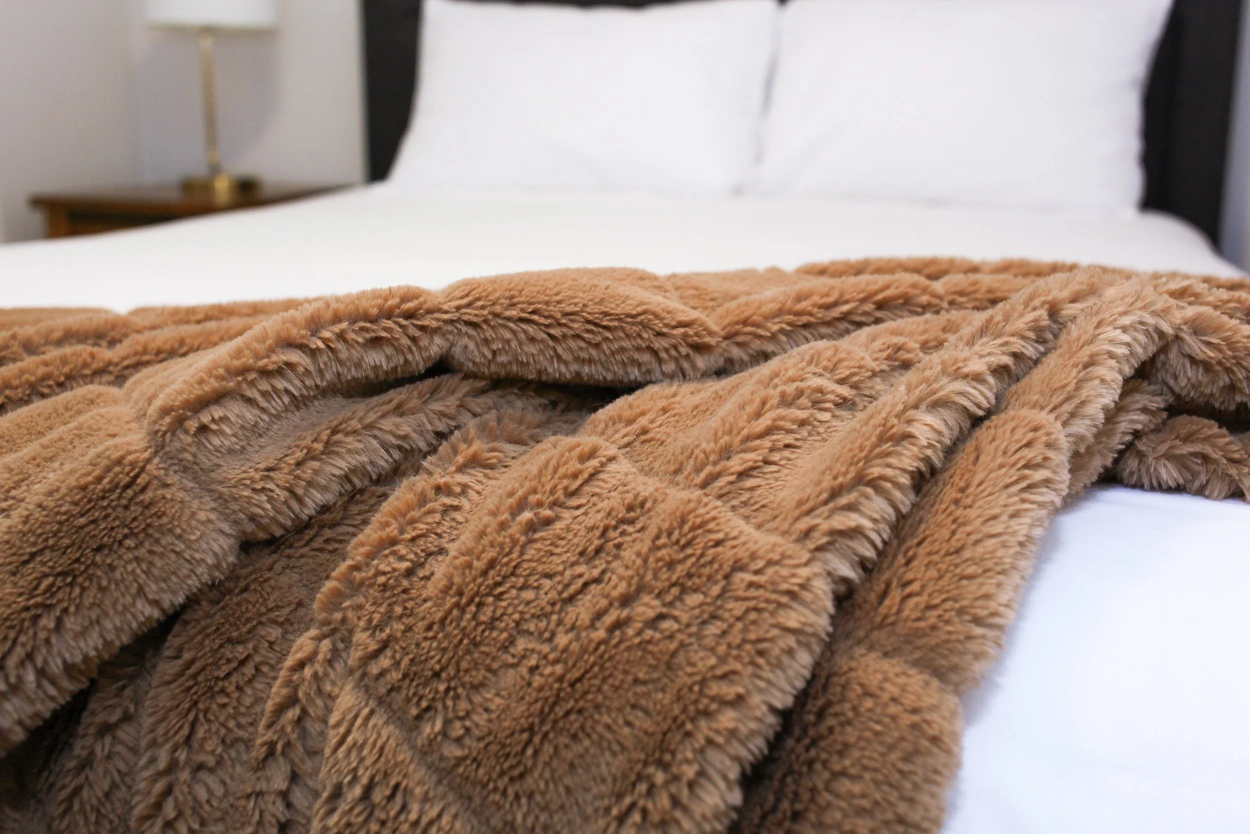 A neatly made bed with white sheets and pillows, topped with a soft brown faux fur blanket.