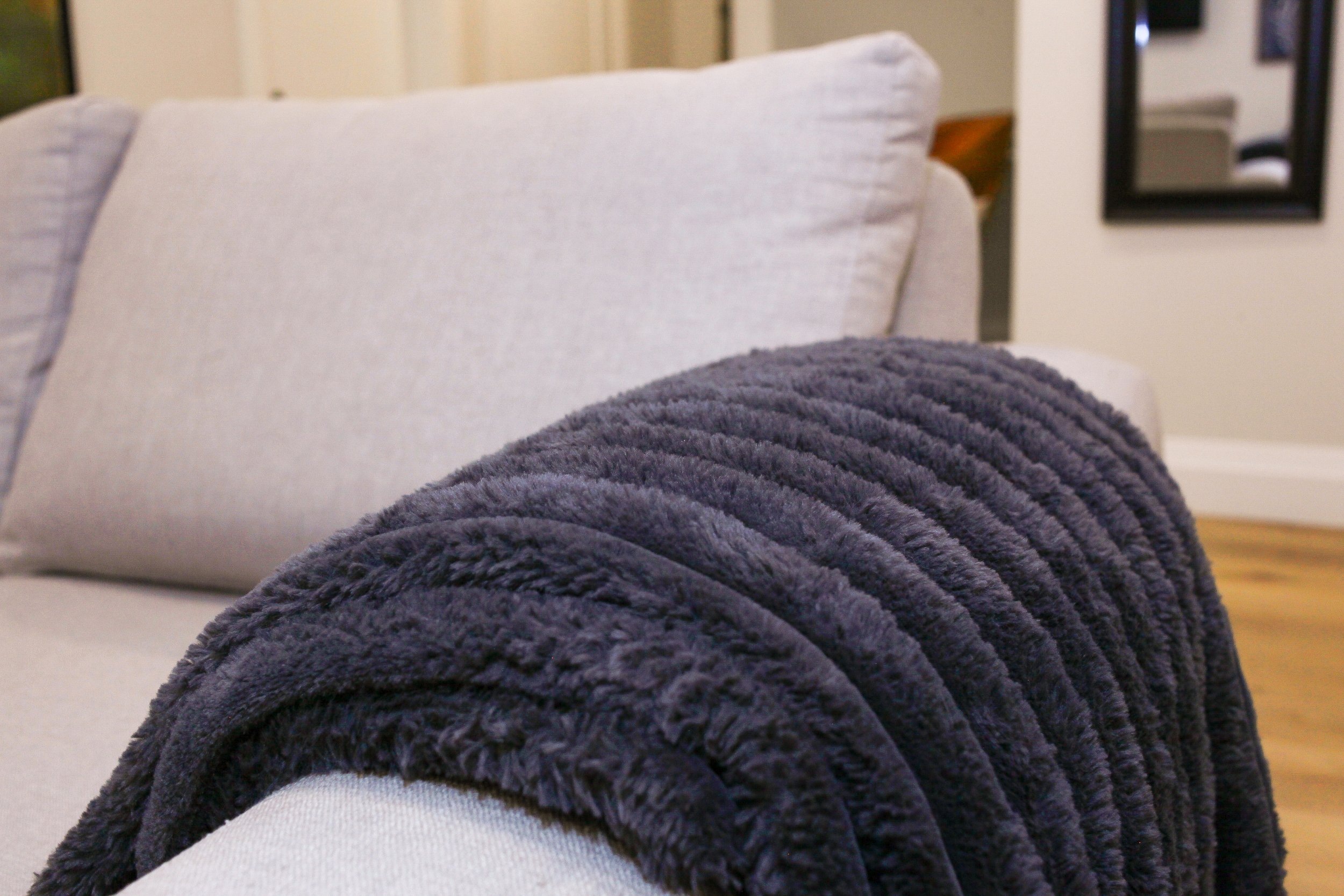 A beige sofa with a dark gray, plush, ribbed throw blanket draped over the armrest.