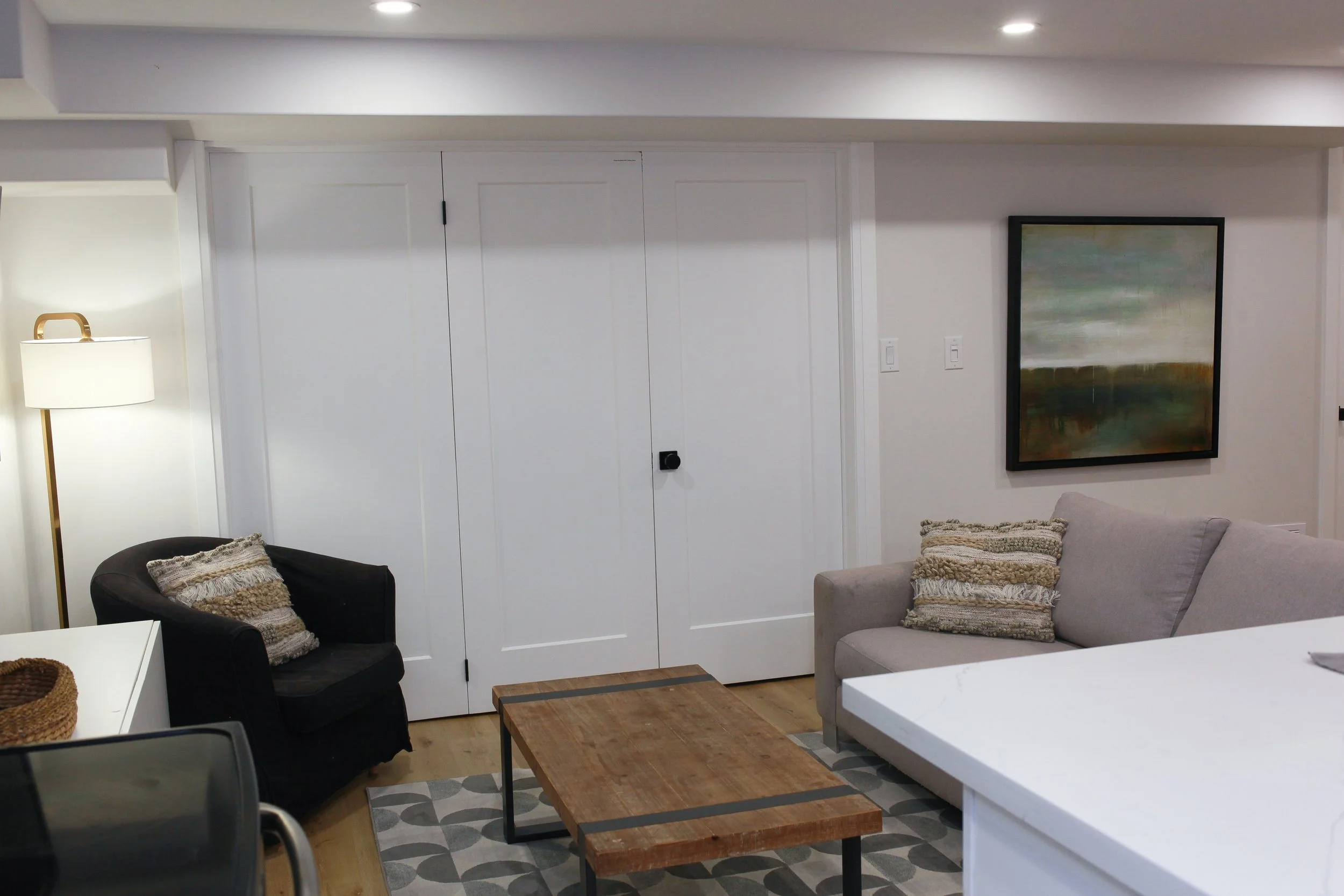 Living room with a gray sofa, black armchair, wooden coffee table, wall painting, and a white lamp, in a cozy modern interior.