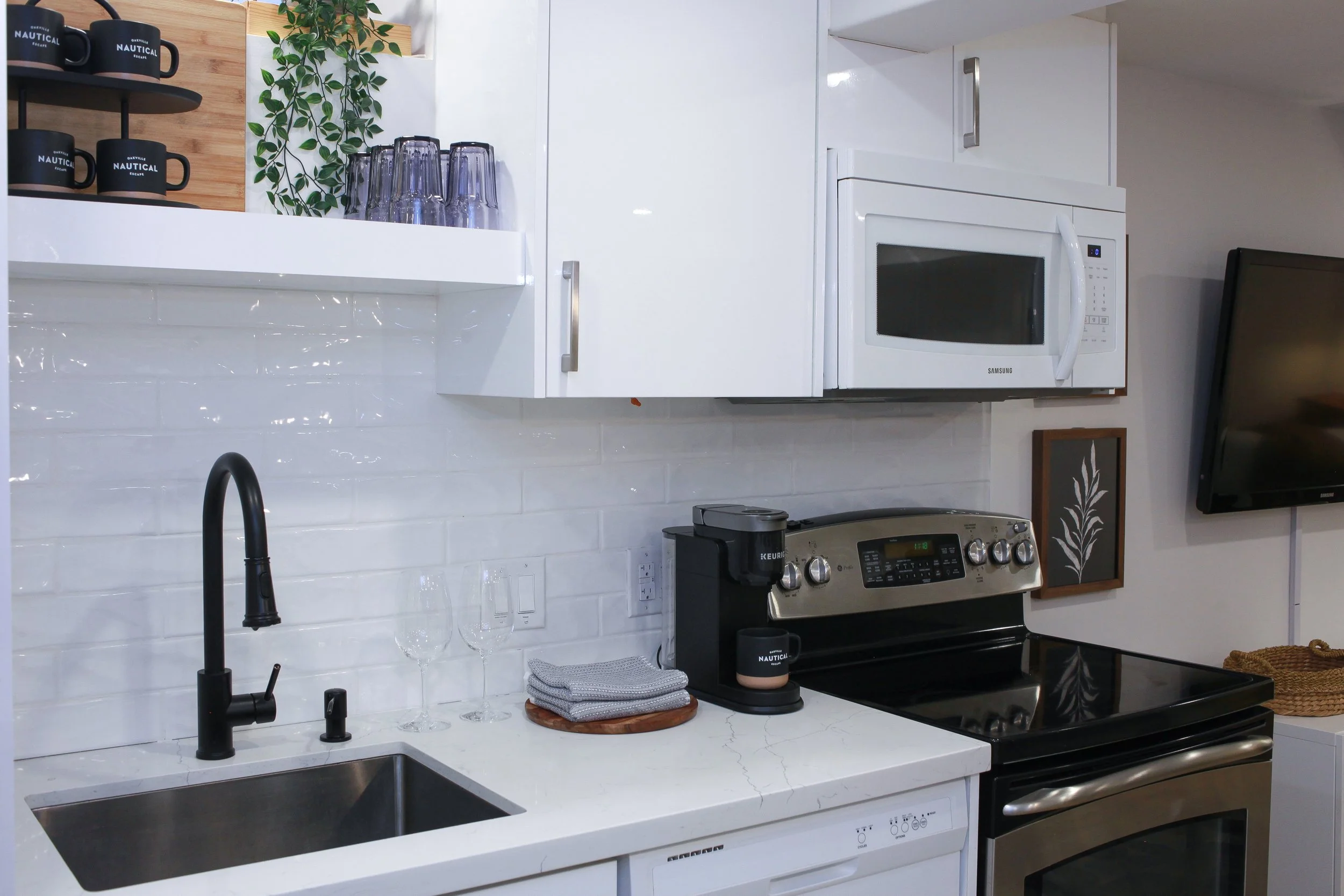 Modern kitchen with white cabinets, black faucet, stainless steel oven, microwave, coffee maker, glassware, and decorative items.