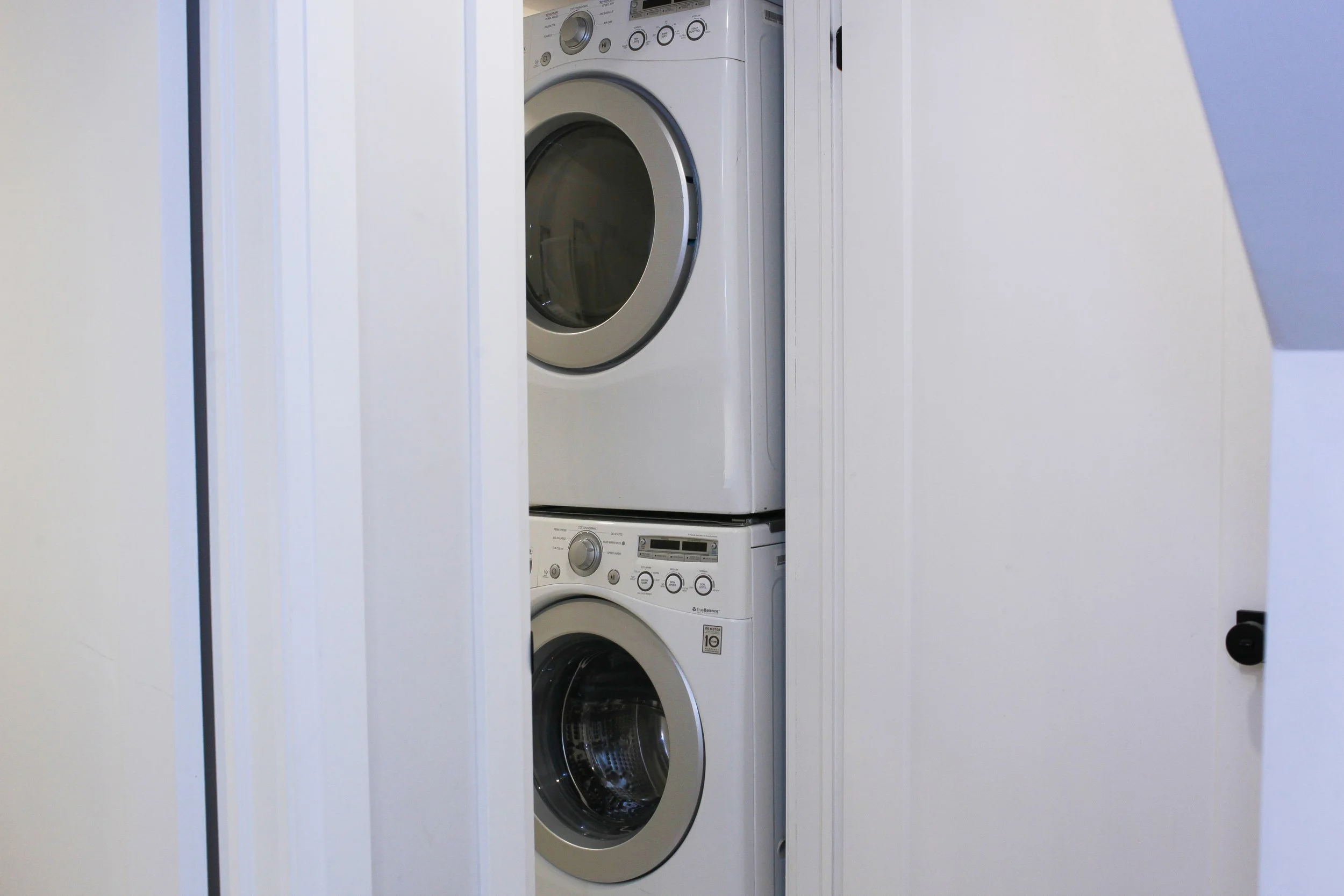 Stacked washer and dryer inside a closet with a partially open door.
