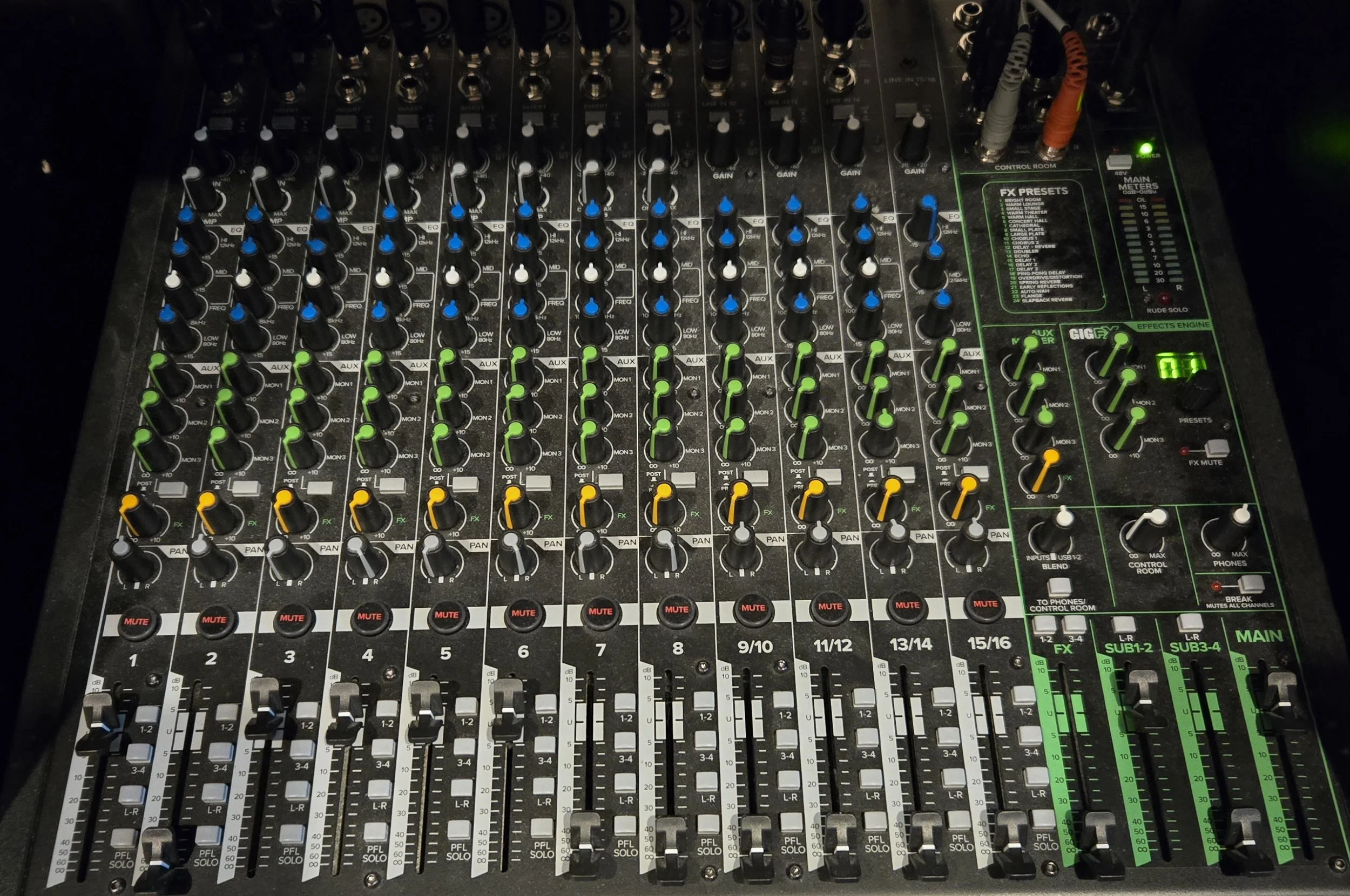 A professional audio mixing console with multiple colorful knobs, sliders, and buttons used for sound control in live music or recording sessions.