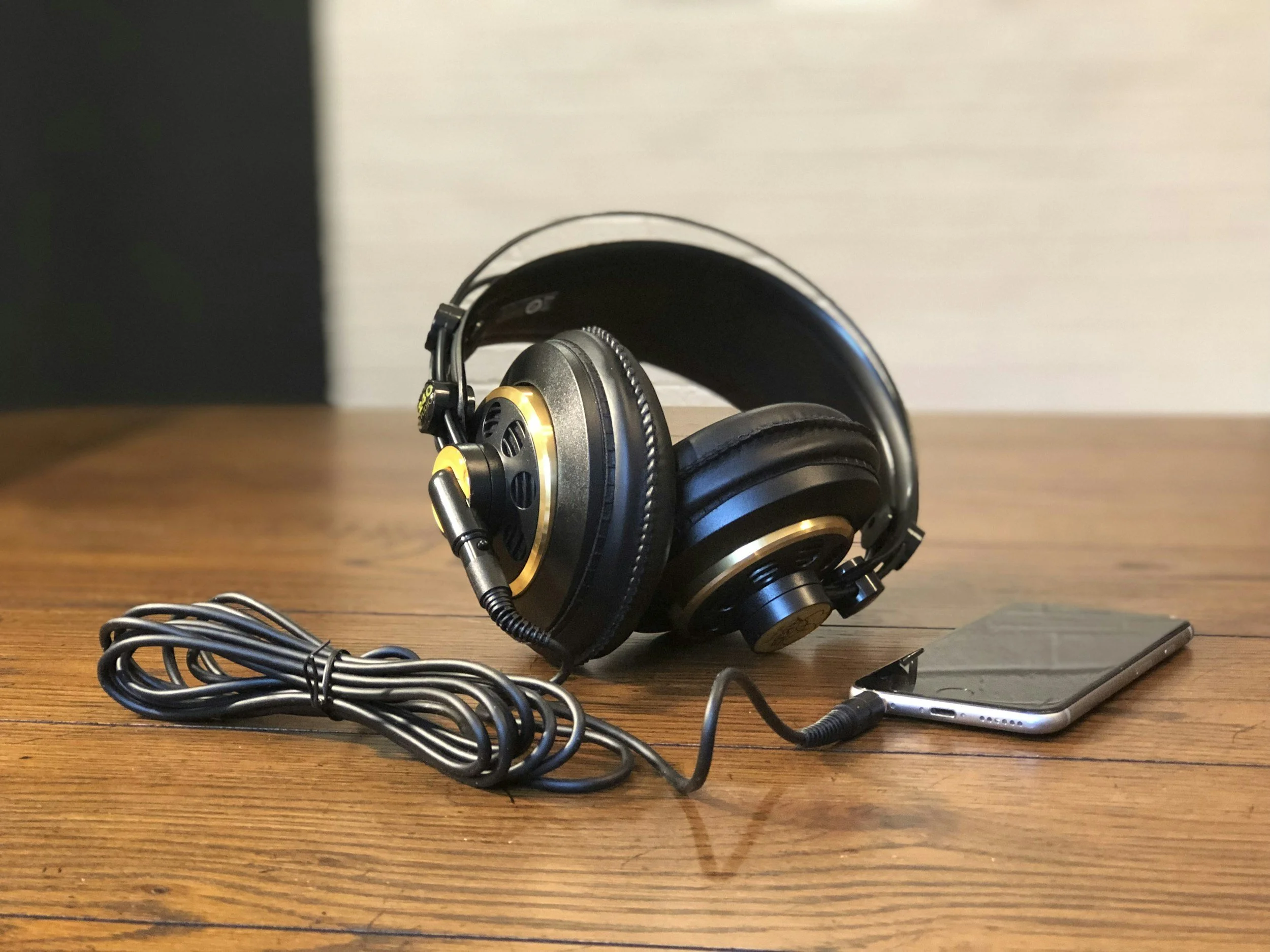 A pair of black over-ear headphones with gold accents connected to a smartphone on a wooden surface.