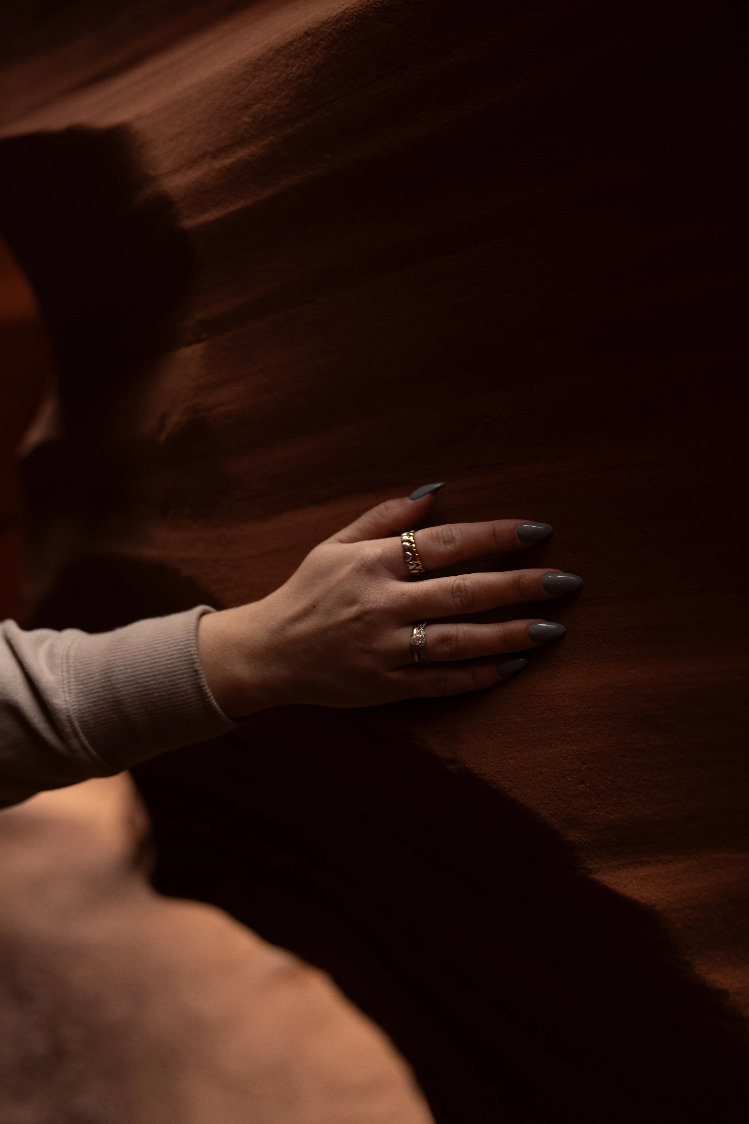 A person with painted gray nails and wearing rings is touching a brown textured surface or fabric.