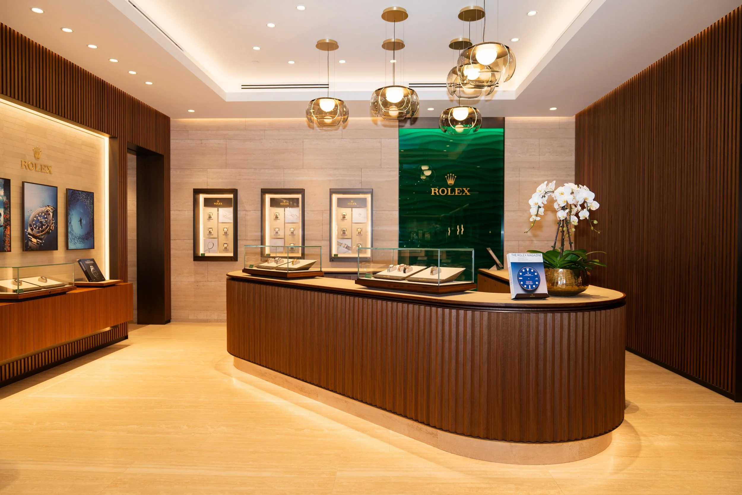 Inside a Rolex store, showing display cases with watches, framed advertisements, a green Rolex logo on the wall, and modern interior lighting.