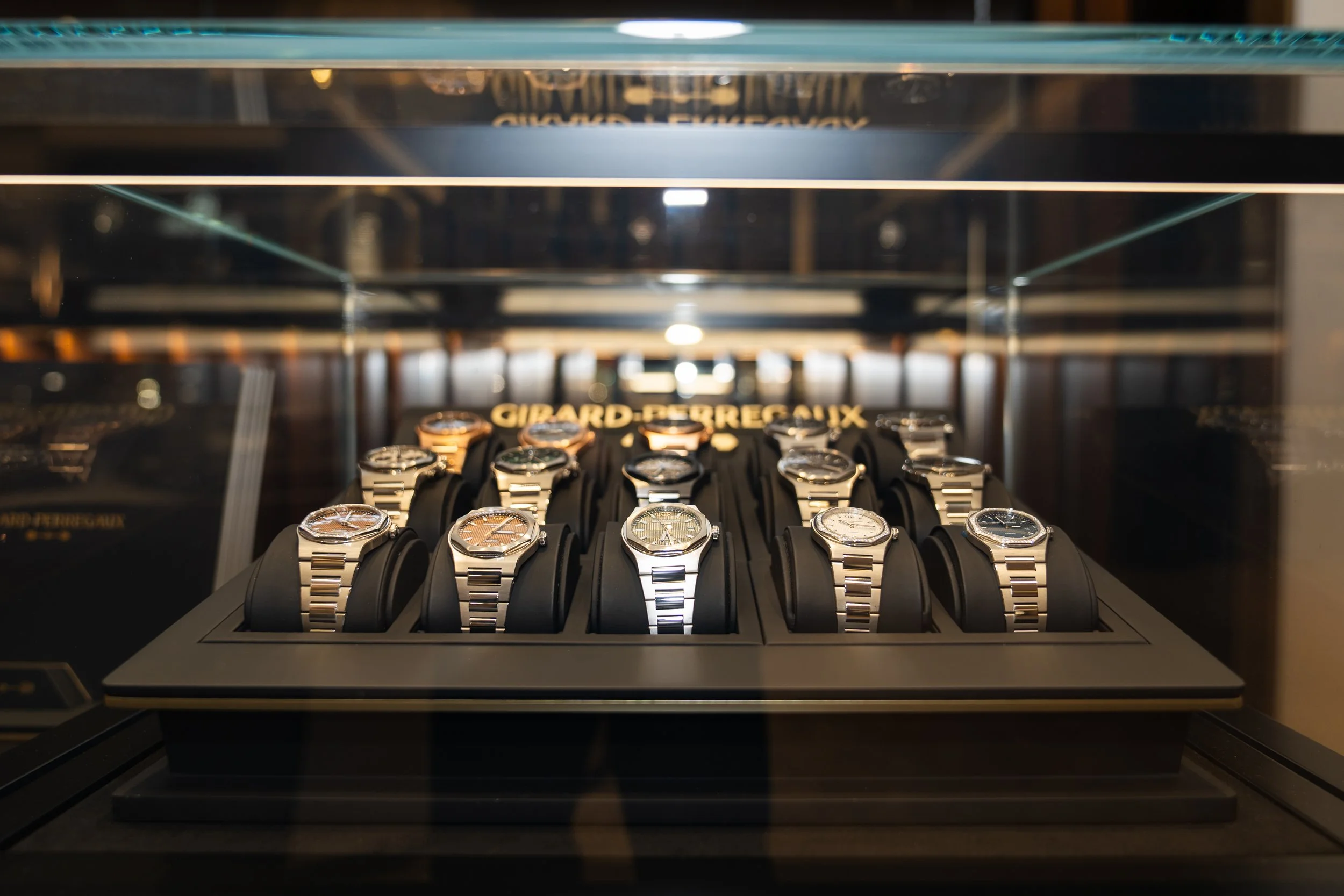 Display case of luxury watches with metal bands, arranged in rows inside a glass showcase.