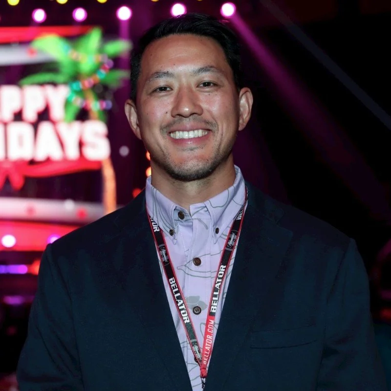 Rich Chou. Man smiling indoors at a festive event with a sign that reads 'Happy Holidays' in the background. Clipping MMA. Scale MMA.