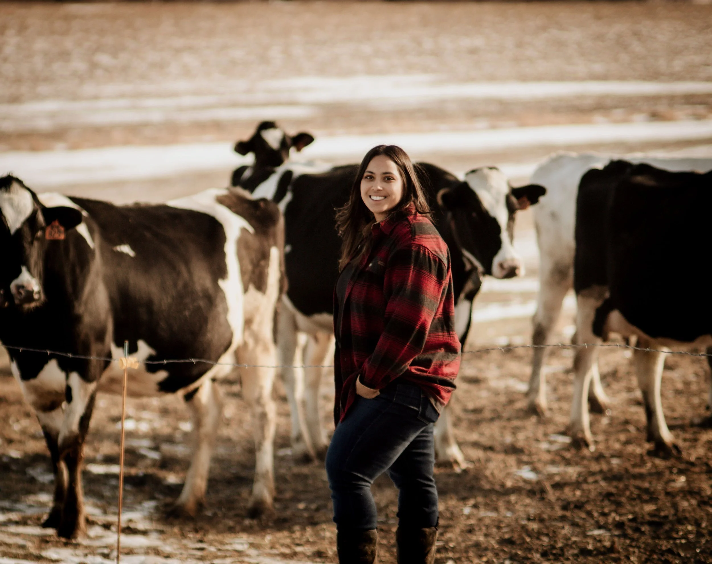 A woman smiling and standing outdoors with cows behind her.