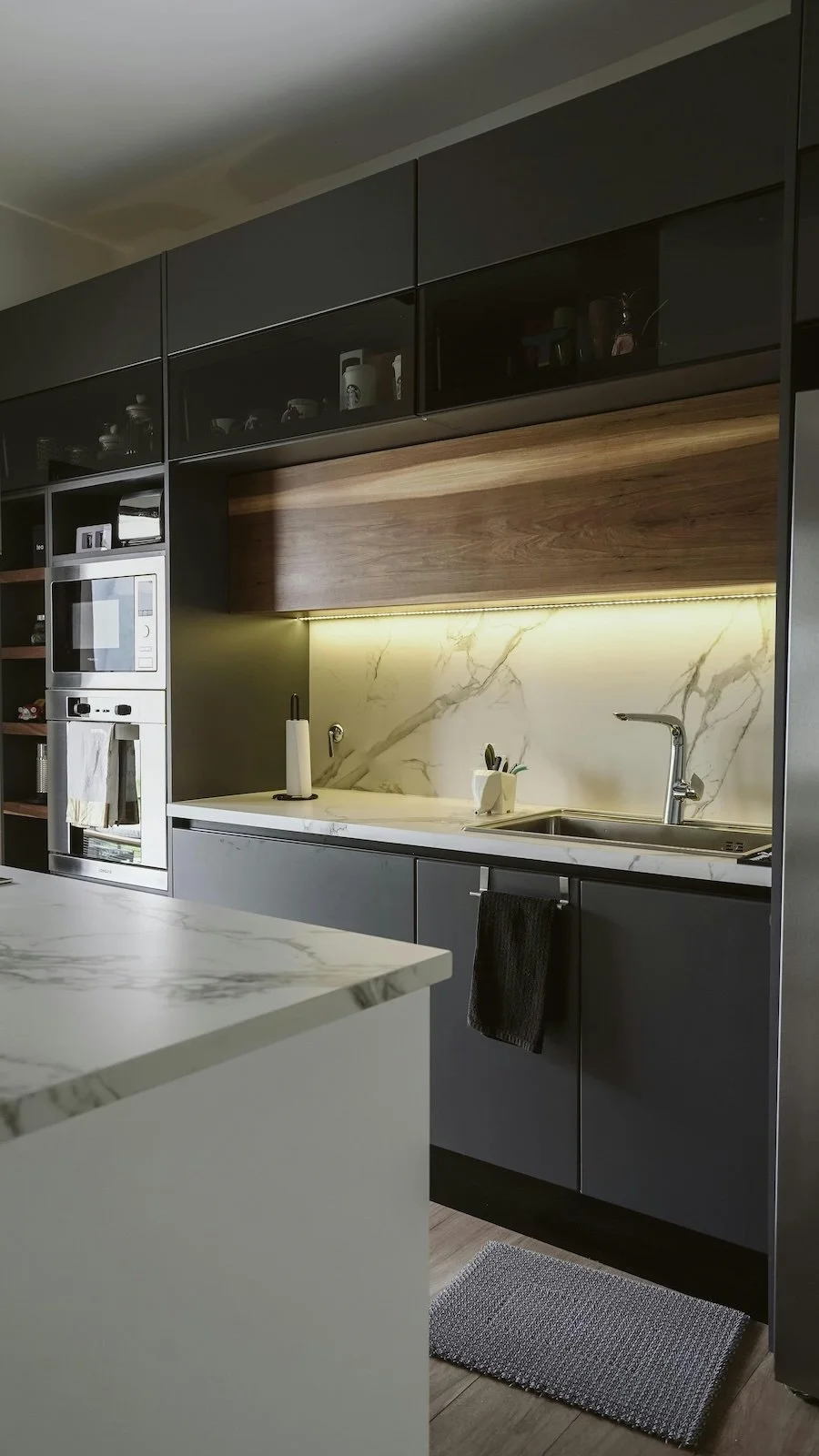Cocina moderna con encimera de mármol, gabinetes grises, y una pared de mármol con iluminación