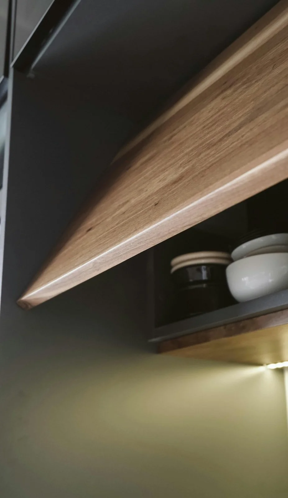 Vista de una estantería de madera con platos y tazones blancos y oscuros.