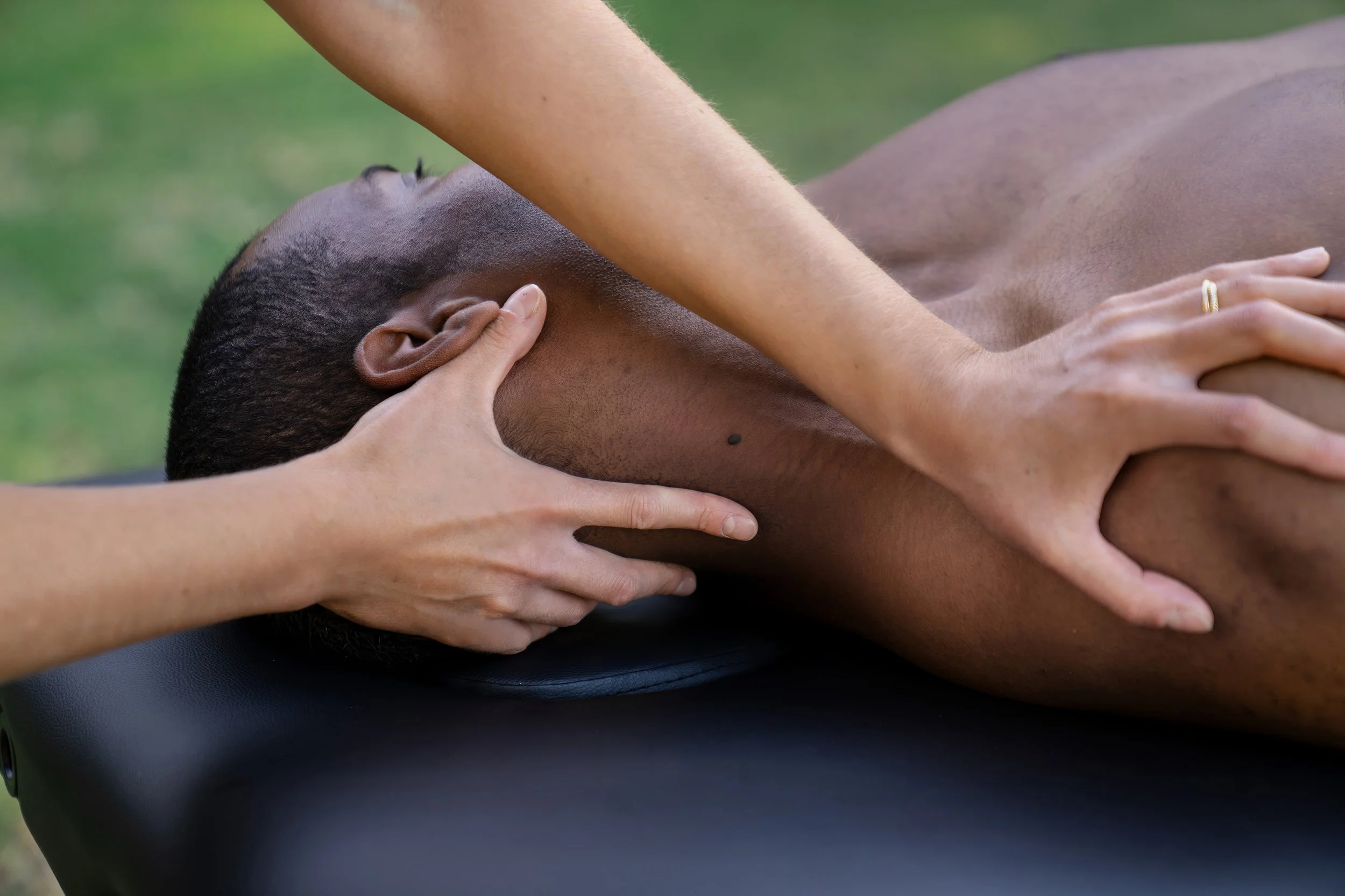 Person receiving a back massage outdoors on a black massage table.