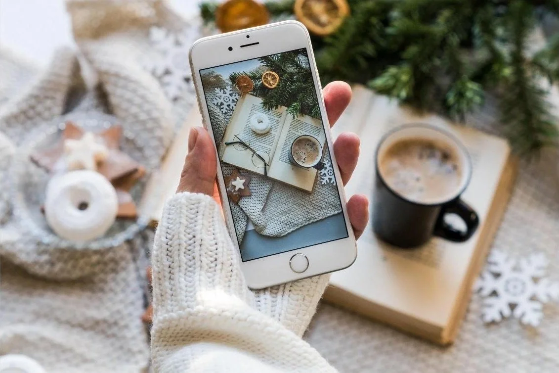 Personne prenant en photo des livres, des lunettes, une tasse de café et des décorations de Noël sur une table
