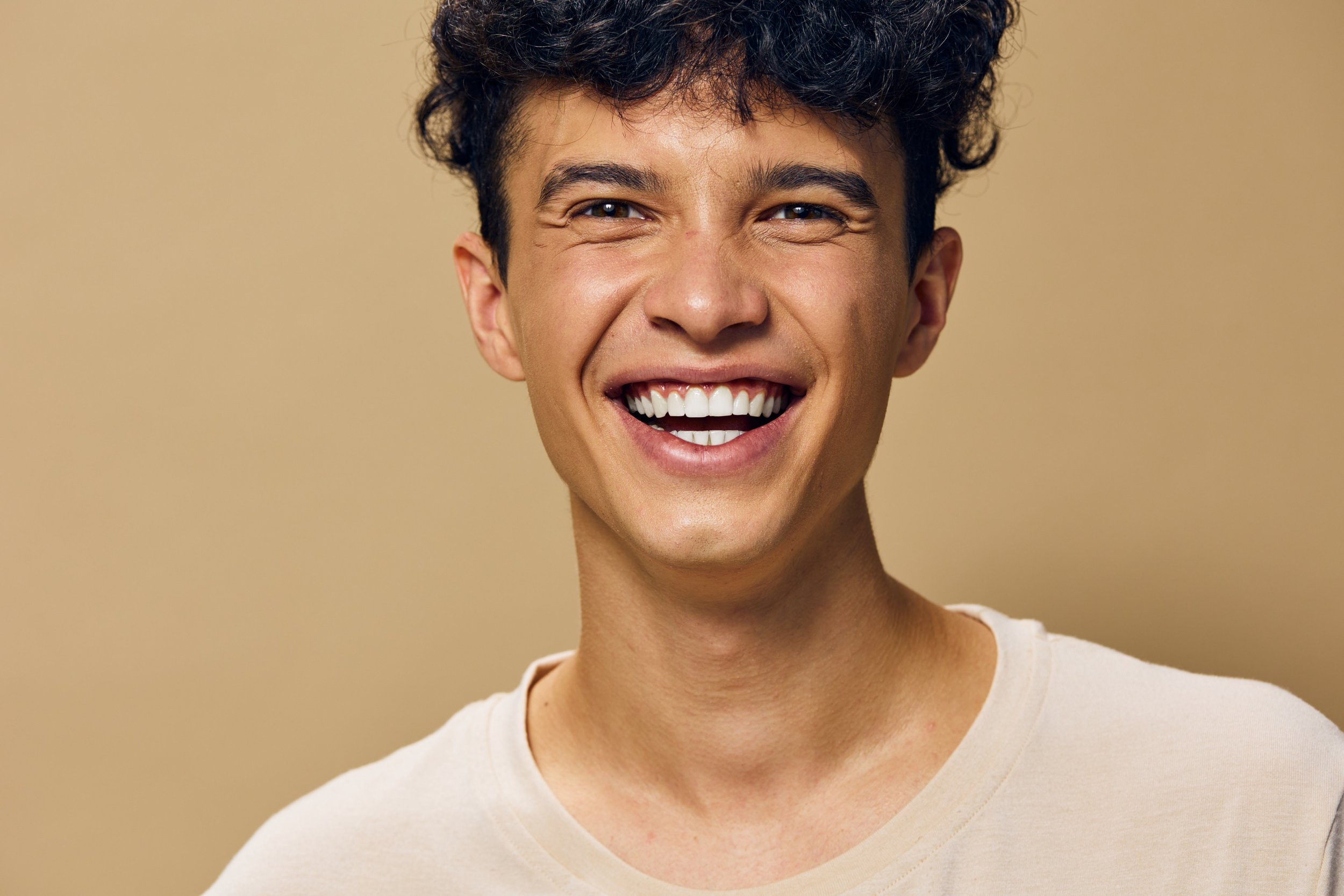 A young teenager smiling broadly with curly hair, wearing a white shirt after his hygienist appointment at Accent Your Dentists