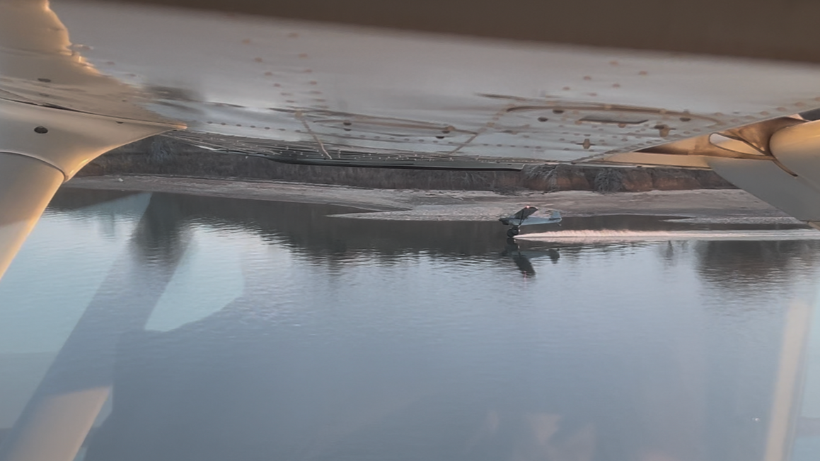 View from under a boat showing the water surface and shoreline in the distance with a boat moving across the water.
