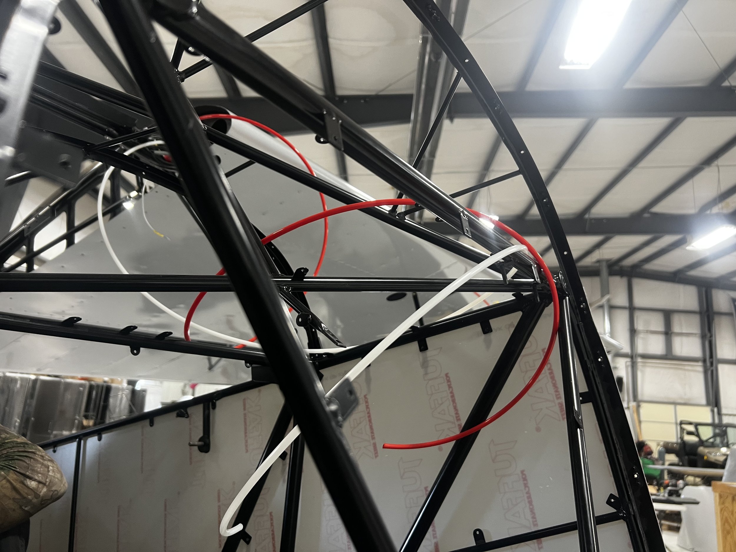 Close-up view of the internal frame of an aircraft or UAV under construction, showing black metal structural skeleton with red and white wiring.