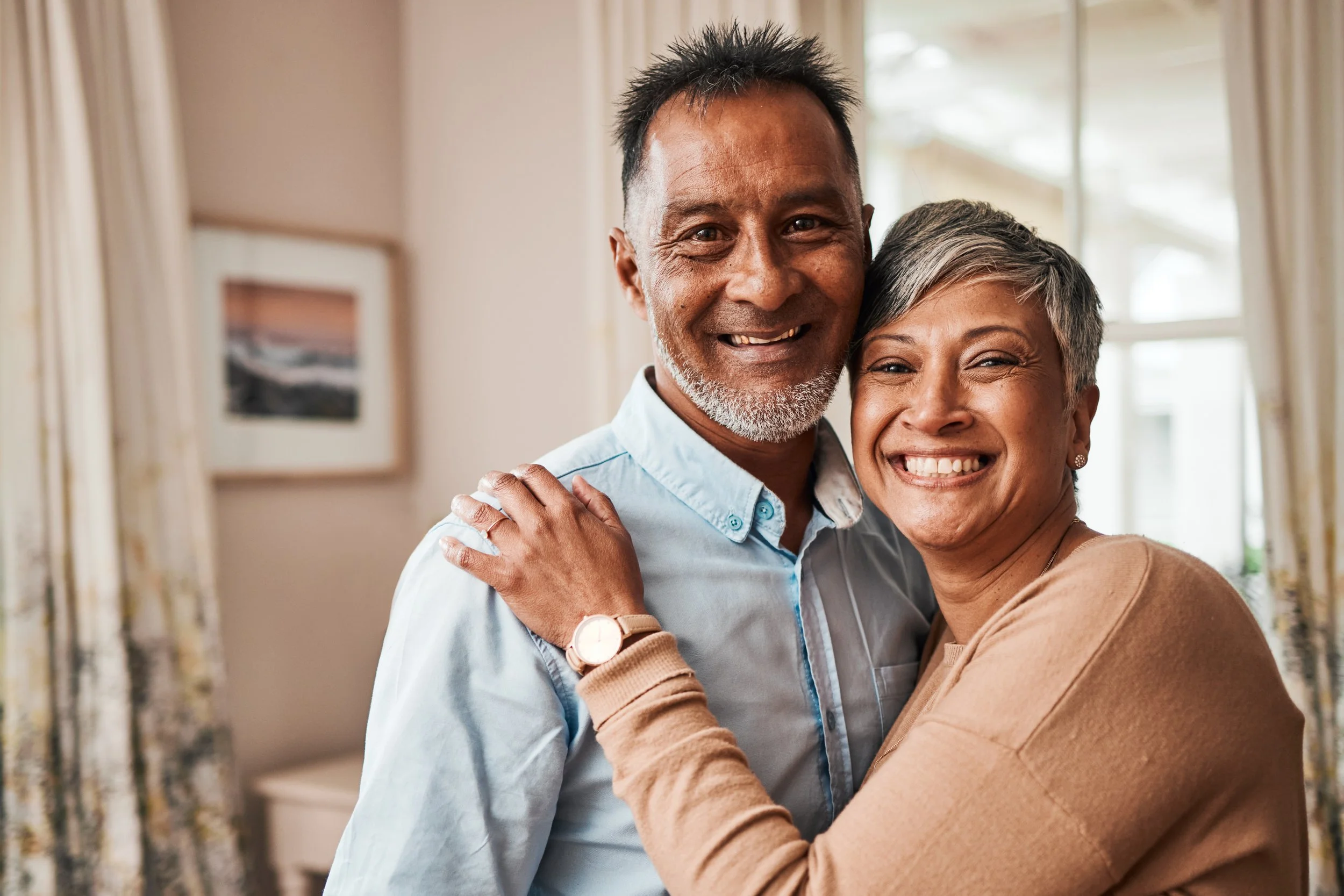A happy middle-aged couple hugging and smiling in a warmly lit living room.