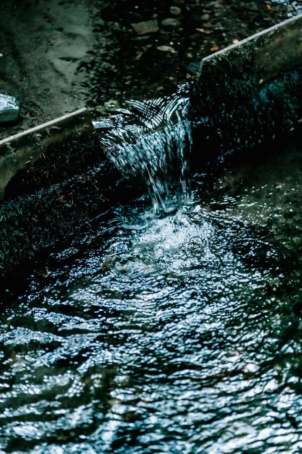 Water flowing between two concrete barriers, creating ripples in a water channel.