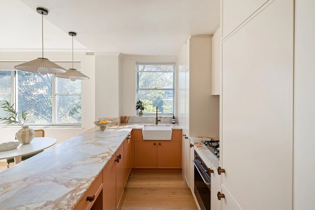 Kitchen with marble countertop, white cabinets, window above sink, and stove.